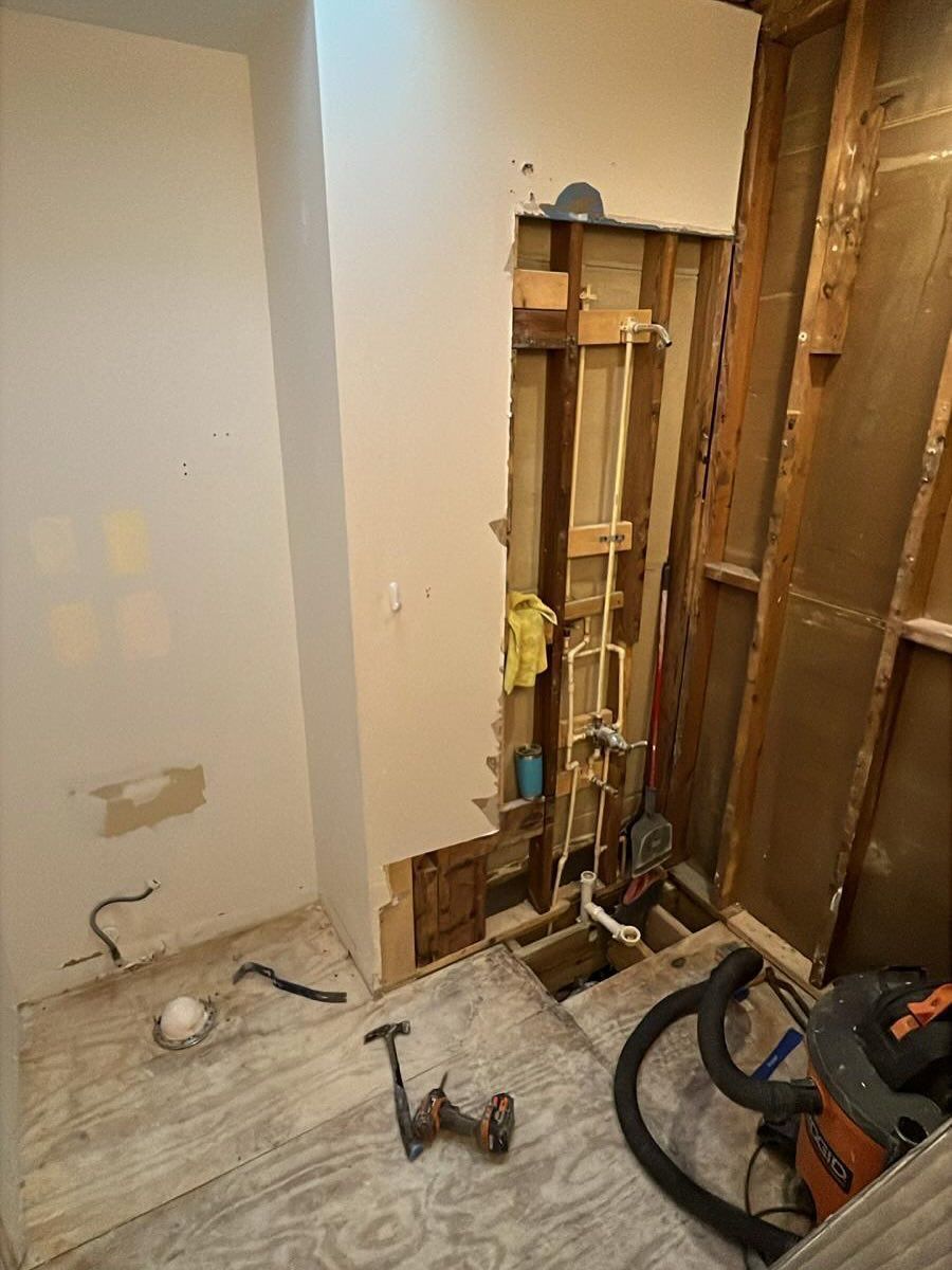 Bathroom under renovation with exposed wall studs, plumbing, and a floor covered in tools and debris