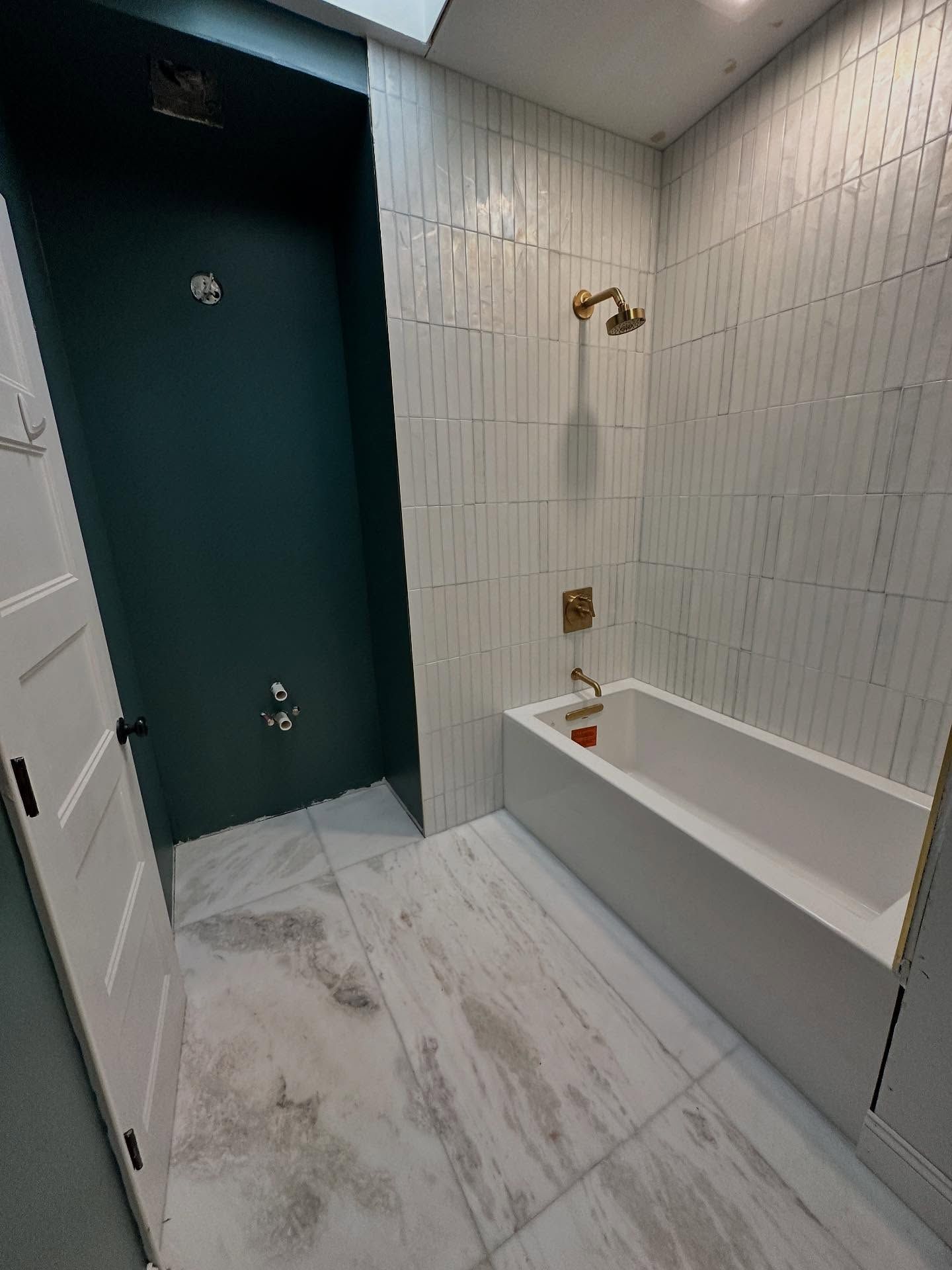 Modern bathroom with dark teal shower door, white tile walls, marble floor, and a bathtub shower combo