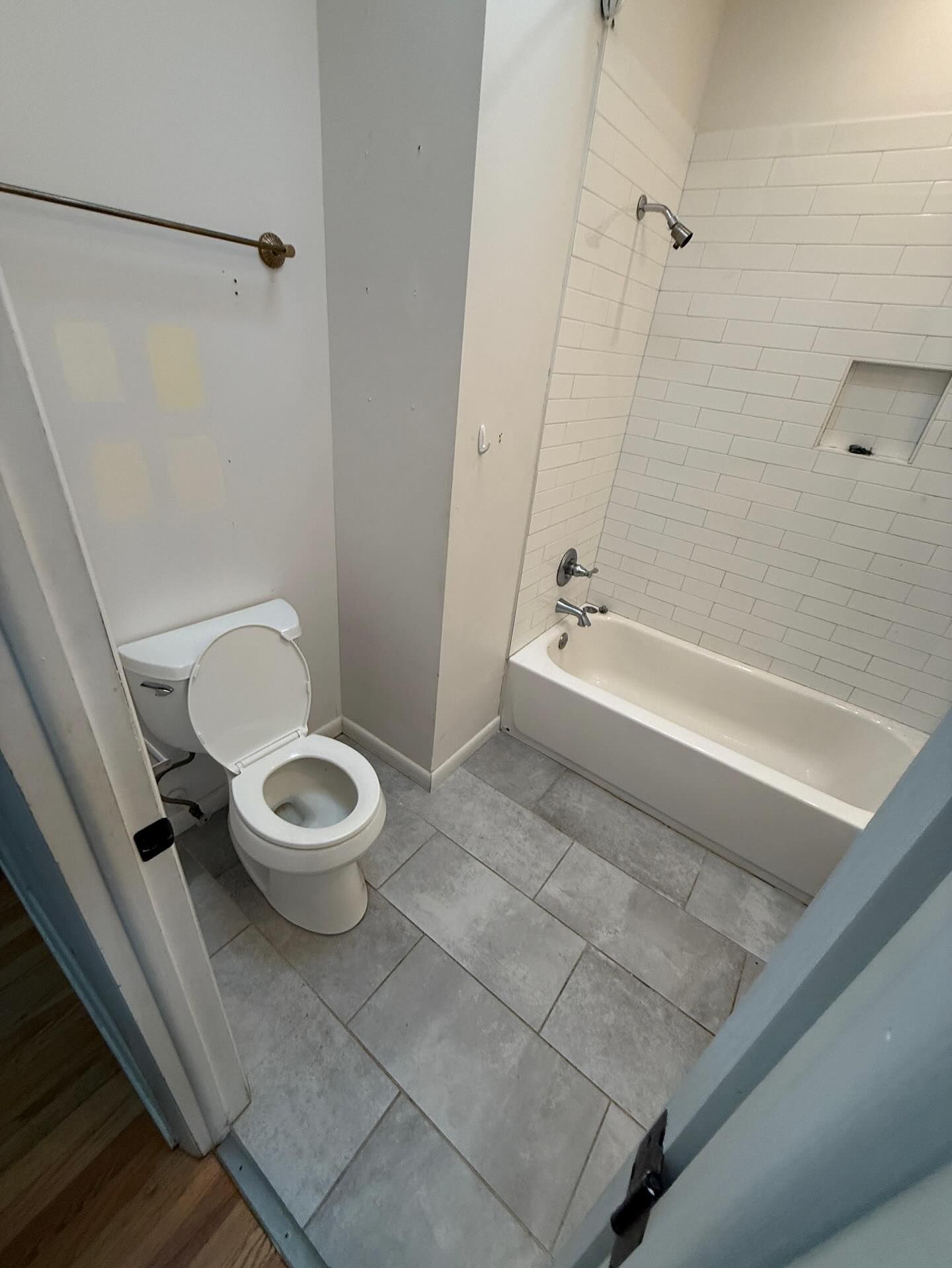 Small bathroom with toilet, white tub, and gray tile floor viewed from the doorway