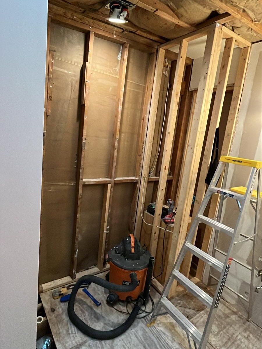 Basement renovation with exposed studs, ladder, and shop vacuum in a partially finished wall area