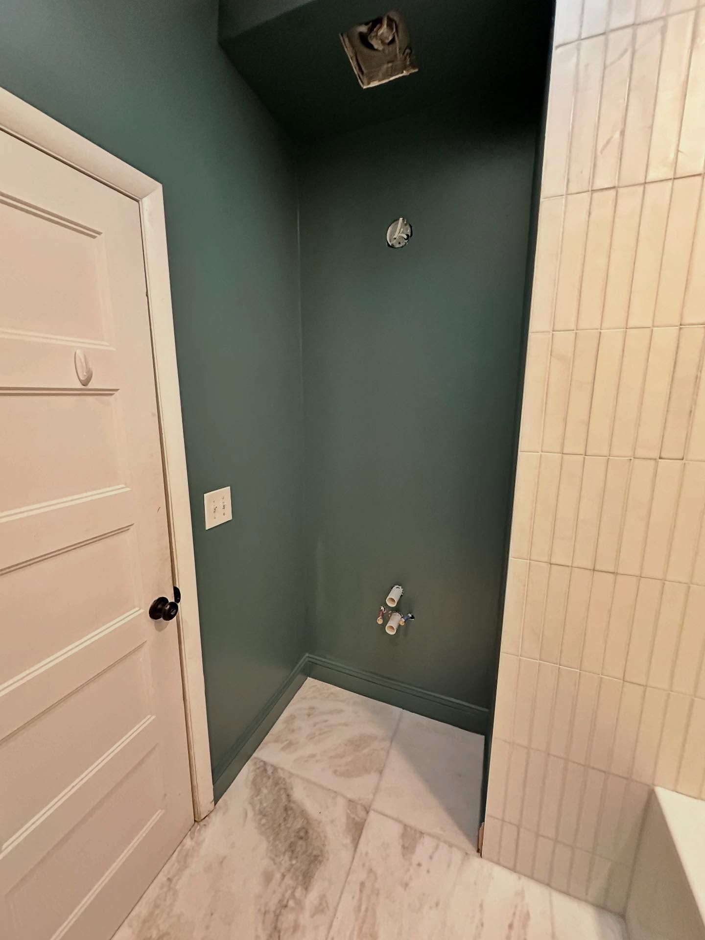 Small bathroom corner with teal walls, white tile floor, shower plumbing, and a white door.