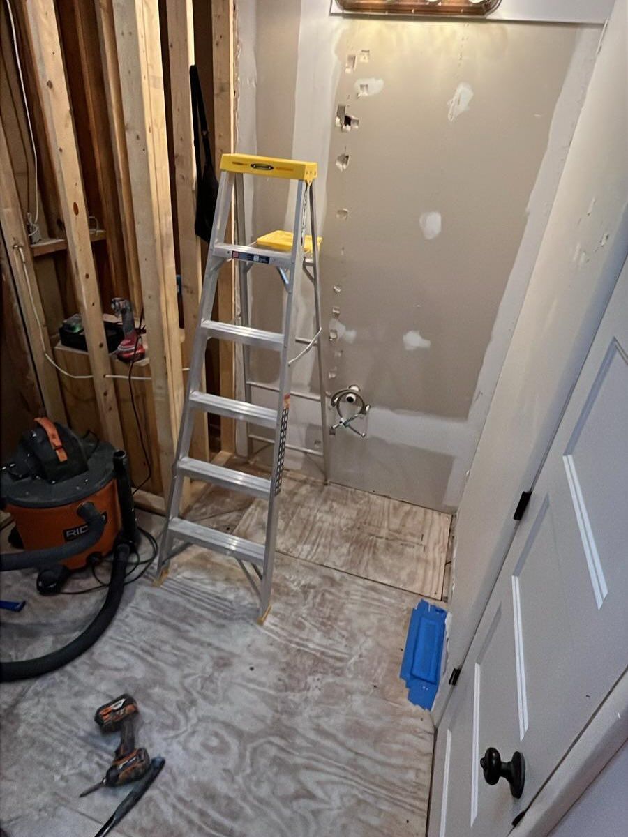 Narrow hallway renovation with ladder, exposed wall studs, tools, and unfinished drywall patching.
