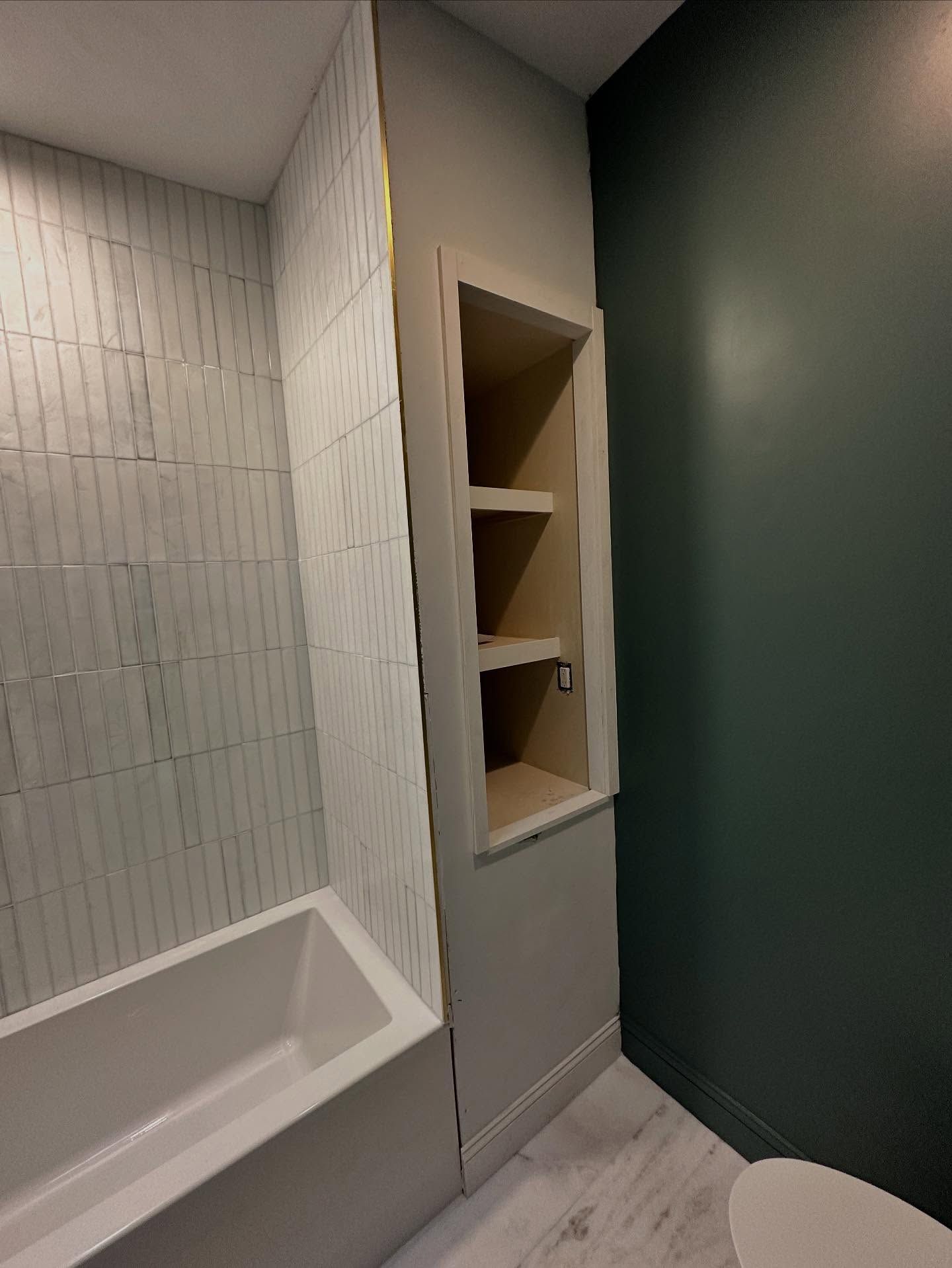 Empty bathroom with white tub, tiled walls, built-in shelf, and dark green door.