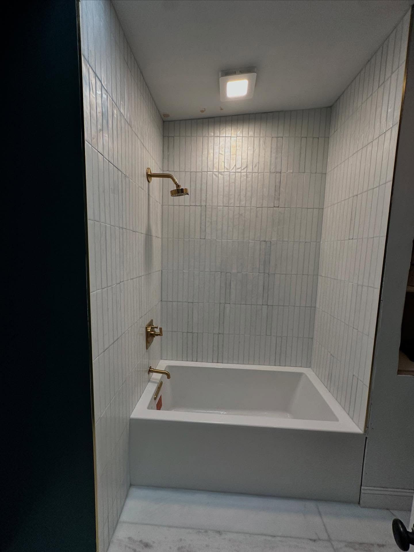 Empty white tiled bathtub alcove with shower fixtures and overhead light