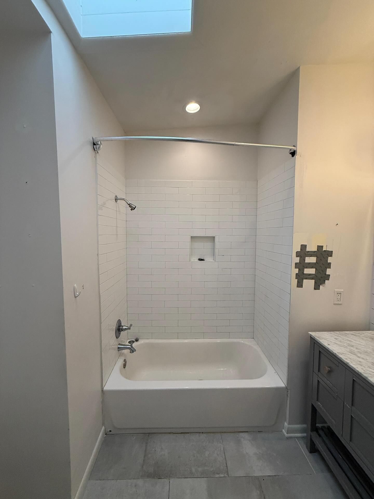 Modern bathroom with a white tub-shower, tiled alcove, skylight, and gray vanity.