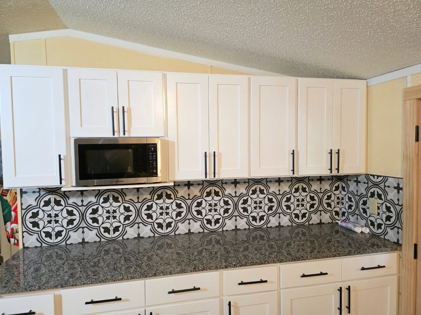White kitchen with cabinets, granite countertop, microwave, and black-and-white patterned tile backsplash