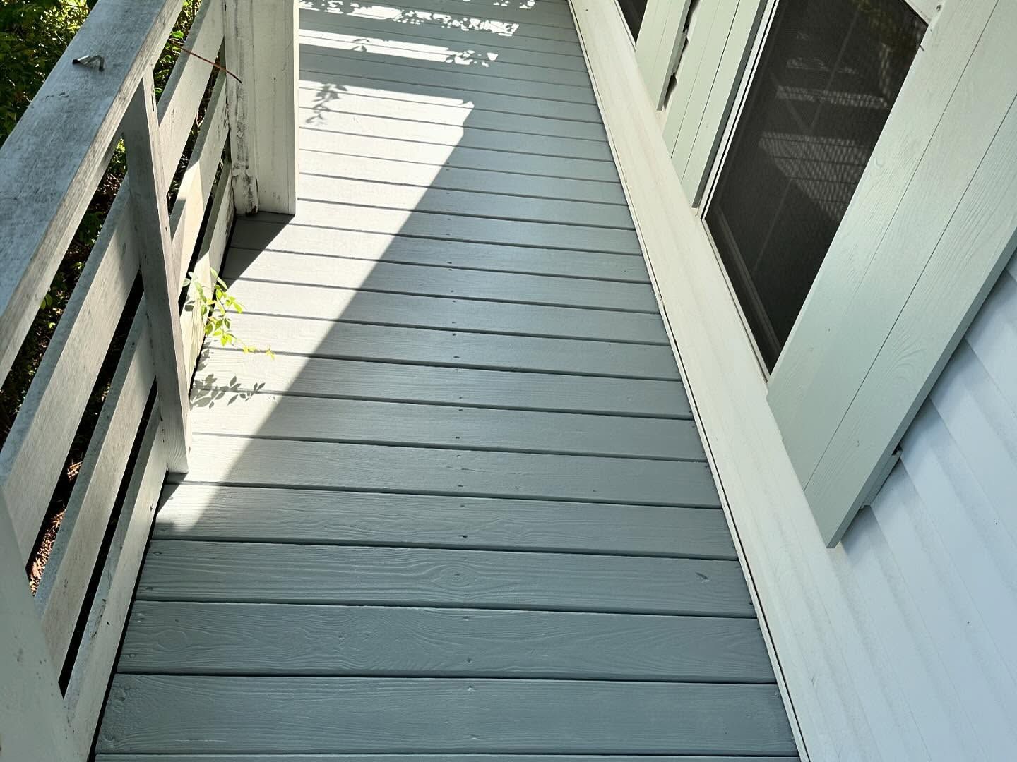 Narrow gray wooden walkway with railings, leading toward a bright sunlit area.