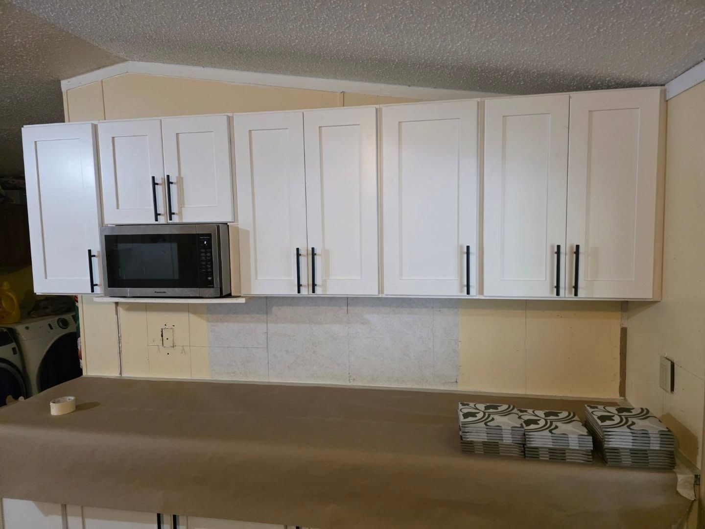 White kitchen cabinets with a microwave and beige countertop in a small kitchen.