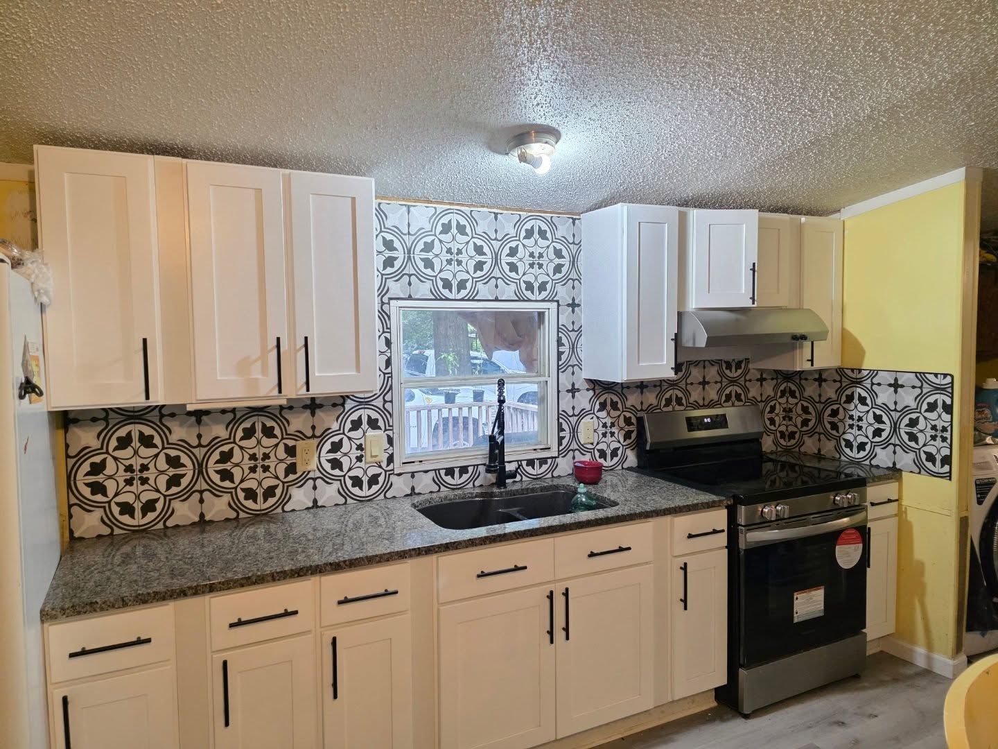 Modern kitchen with white cabinets, black countertops, patterned backsplash, and stainless steel stove under a window