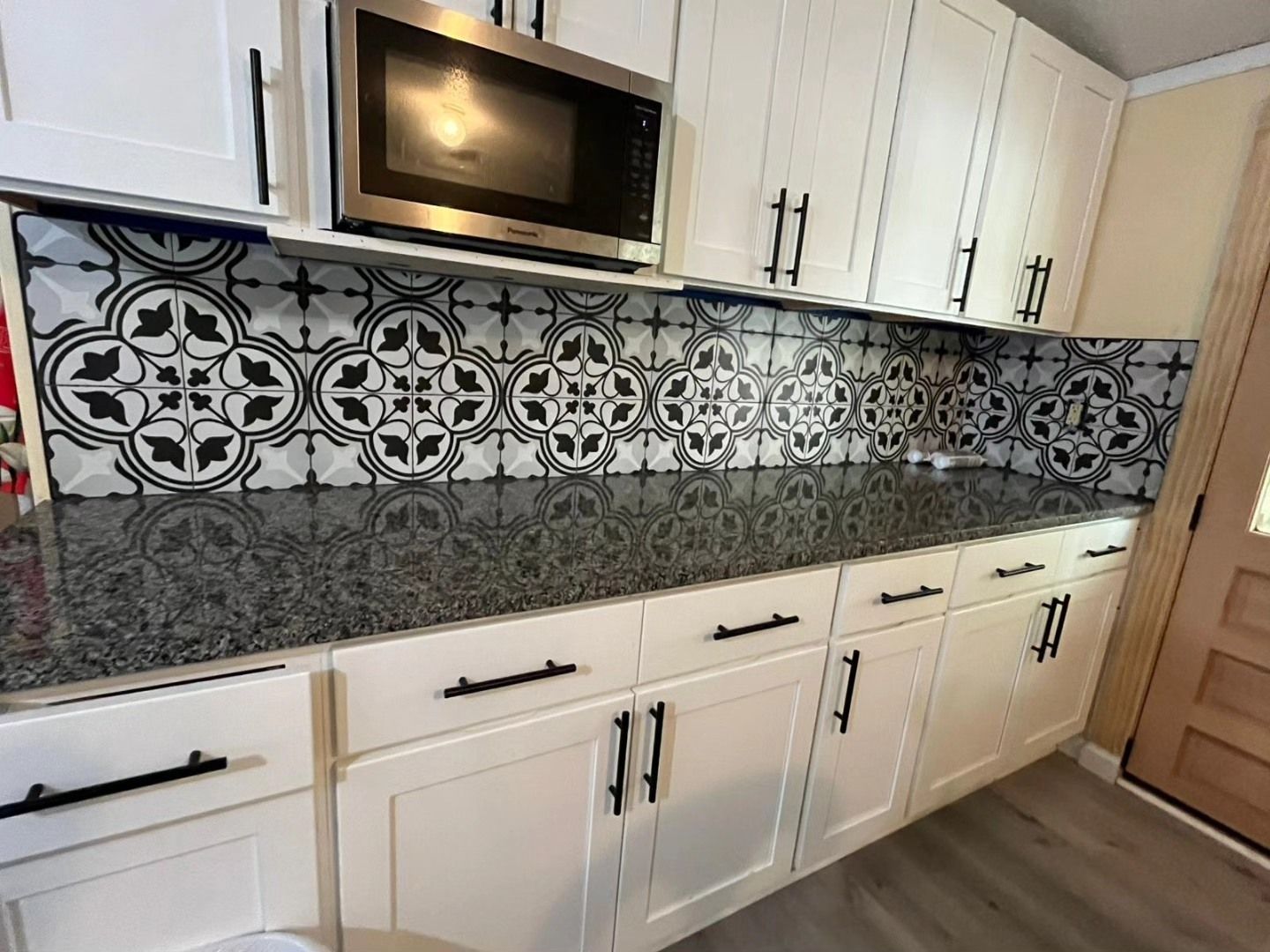 Modern kitchen with white cabinets, black granite countertop, stainless microwave, and black-and-white patterned tile backsplash