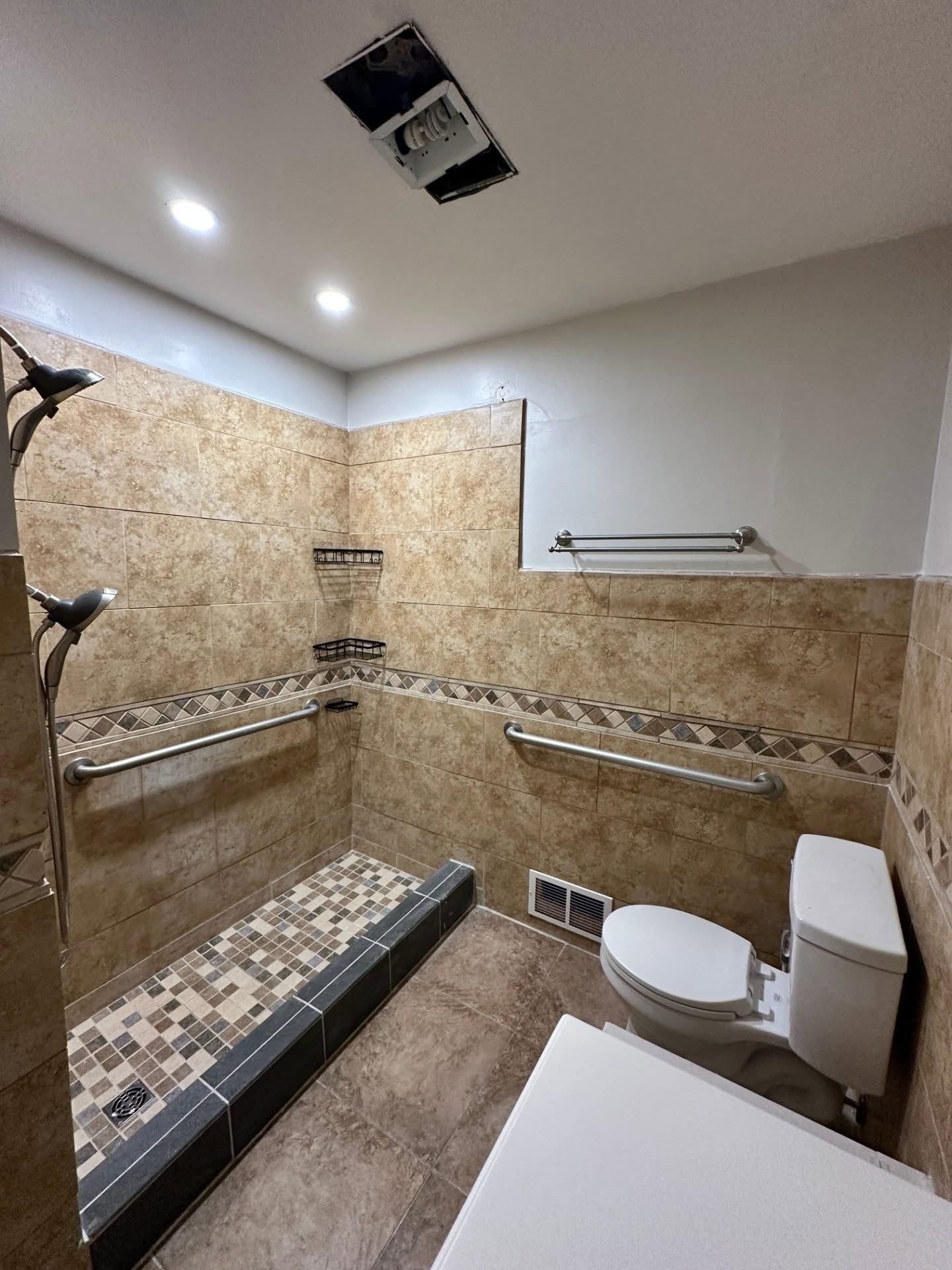 Accessible walk-in shower and toilet in a beige-tiled bathroom with grab bars and shower bench.
