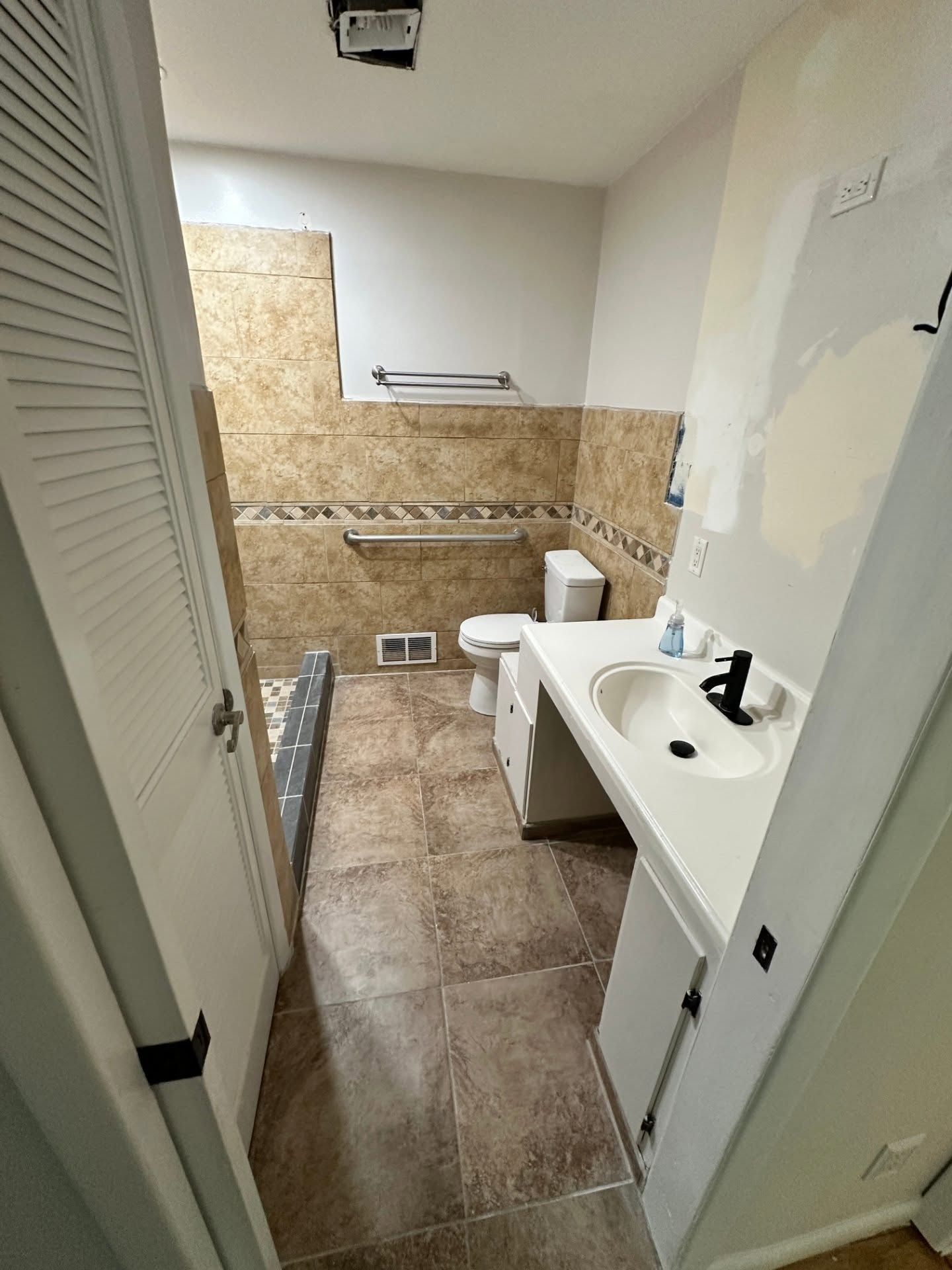 Small bathroom with tan tile, white vanity, toilet, and a shower area under renovation