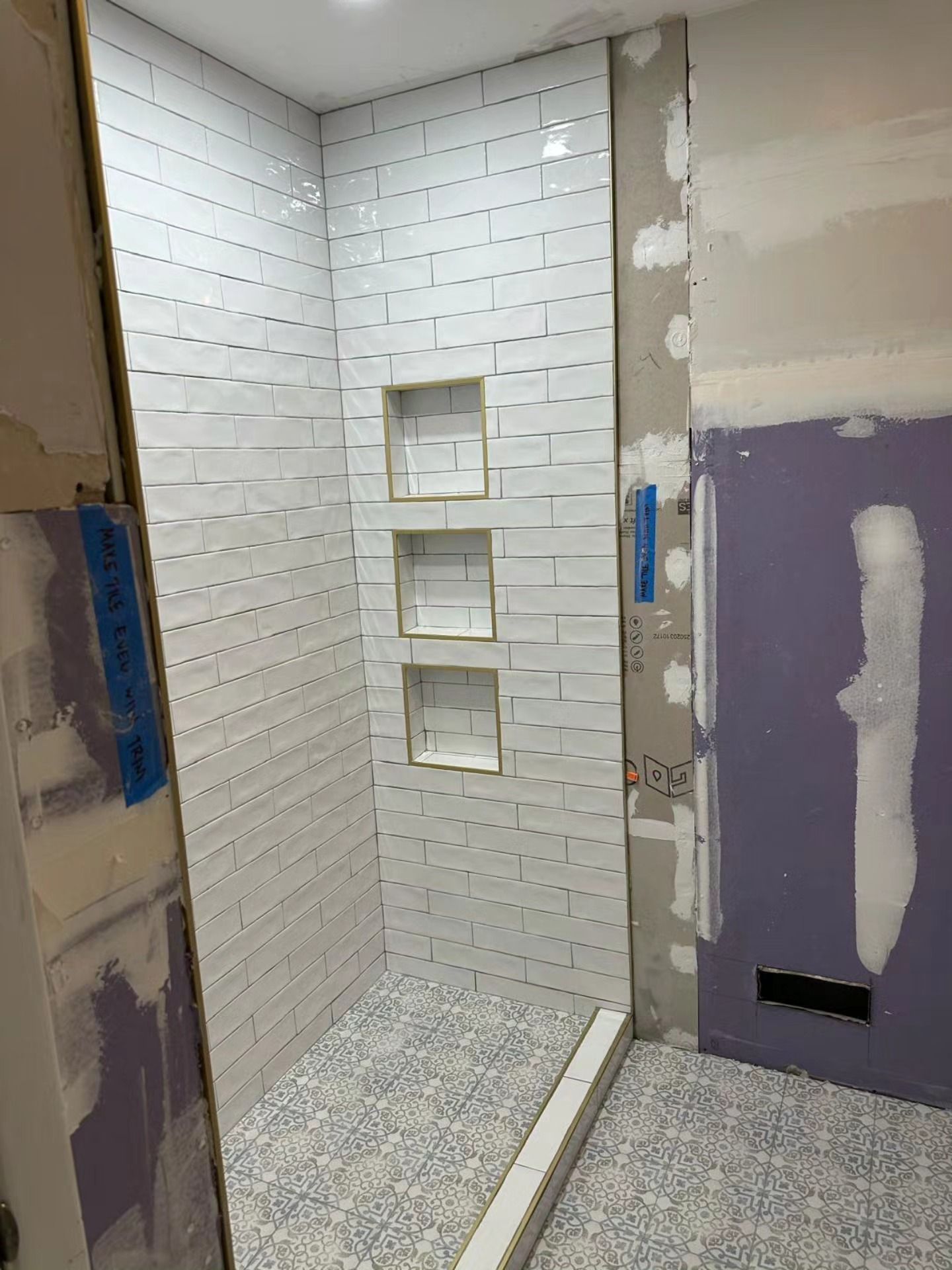Tiled shower under construction with built-in niches and unfinished drywall around the stall
