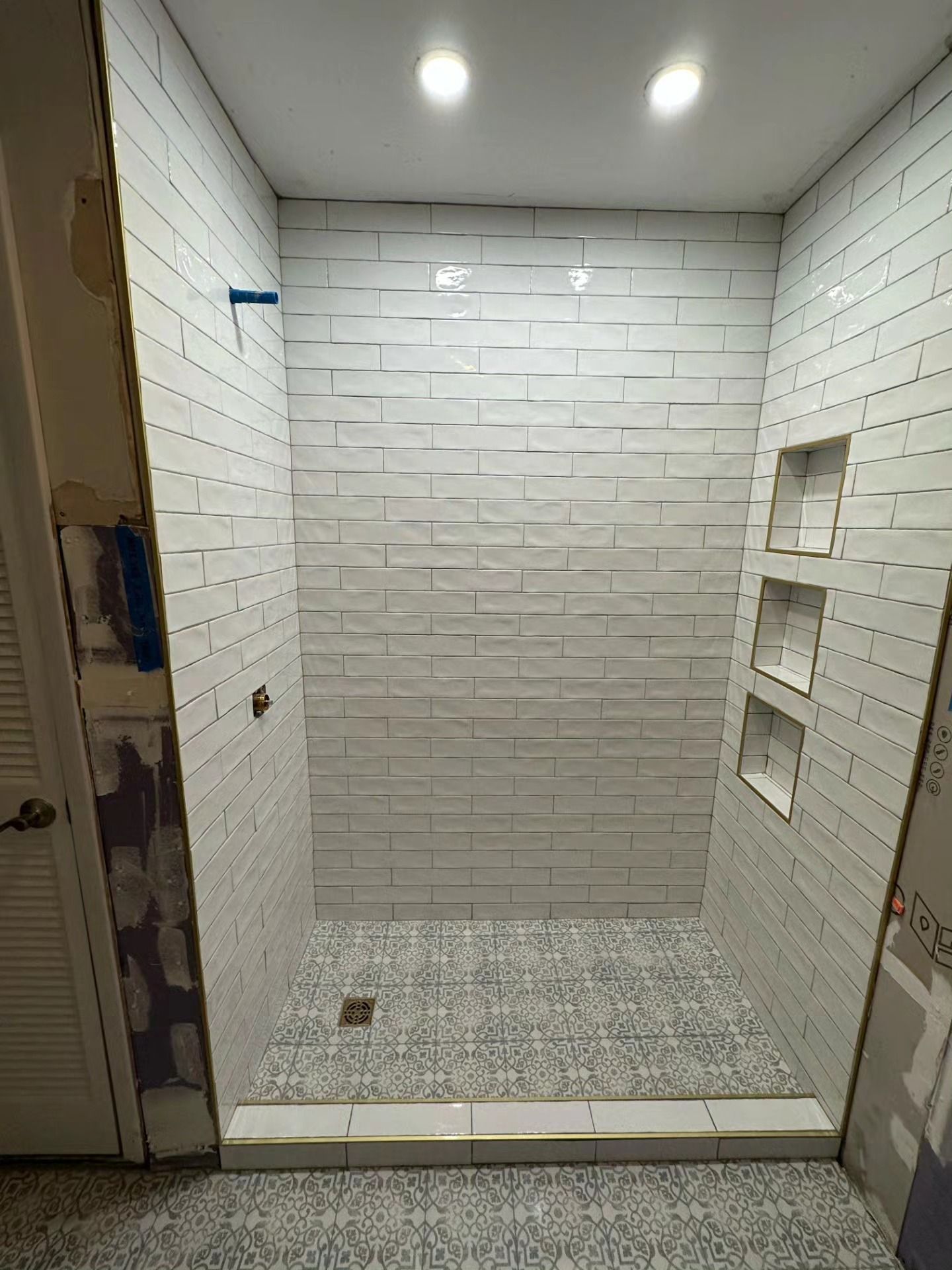 Empty white-tiled shower stall with a tiled floor and built-in wall niches.