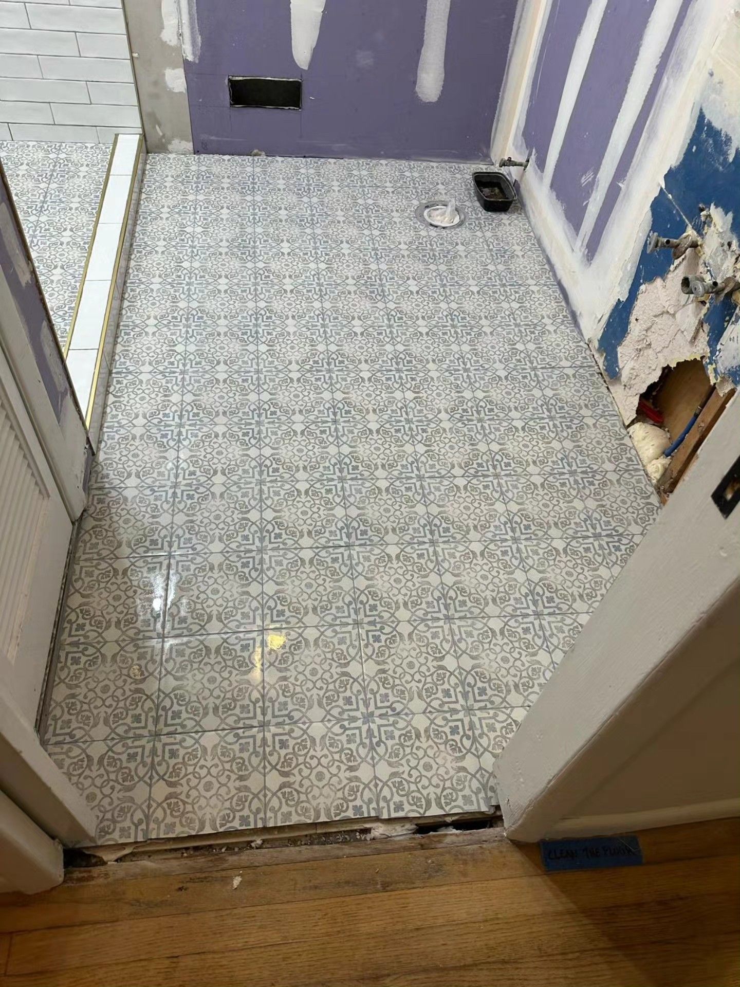 Small tiled room with a purple wall, white brick wall, and a damaged opening near the door.