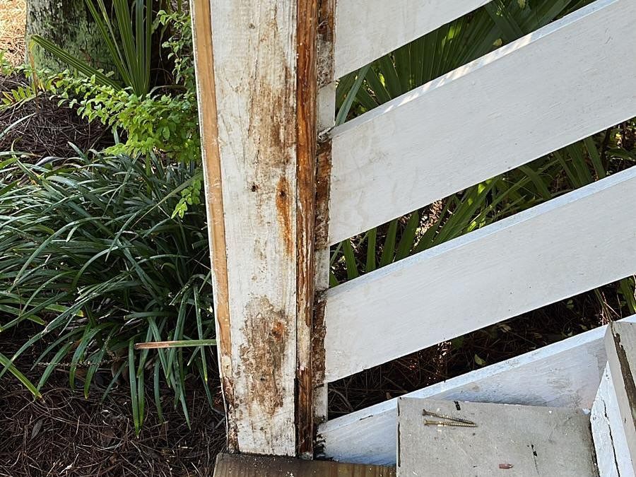 Weathered white wooden gate beside dense green plants and a stone post