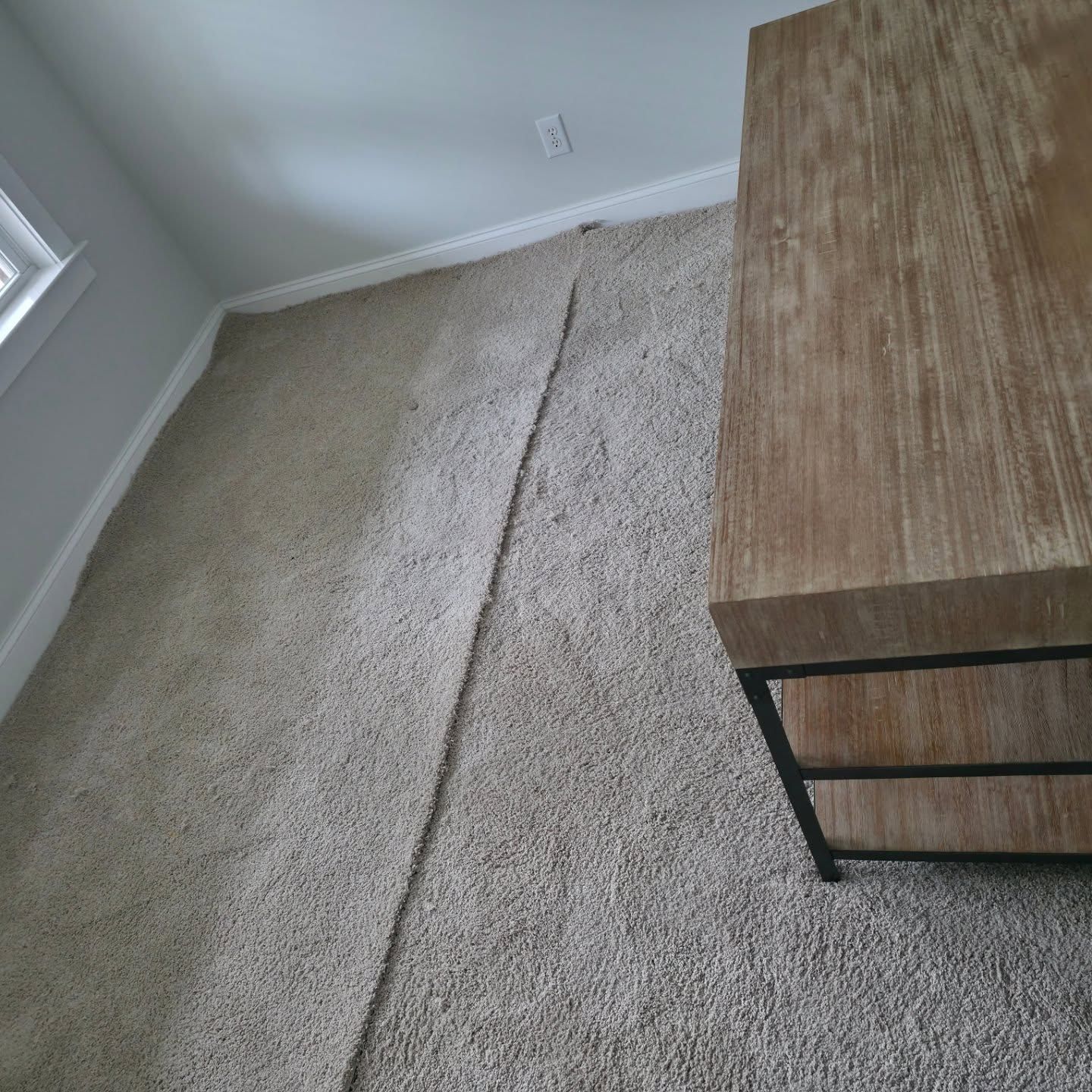 Empty carpeted corner beside a wooden dresser with a visible seam or crack in the carpet