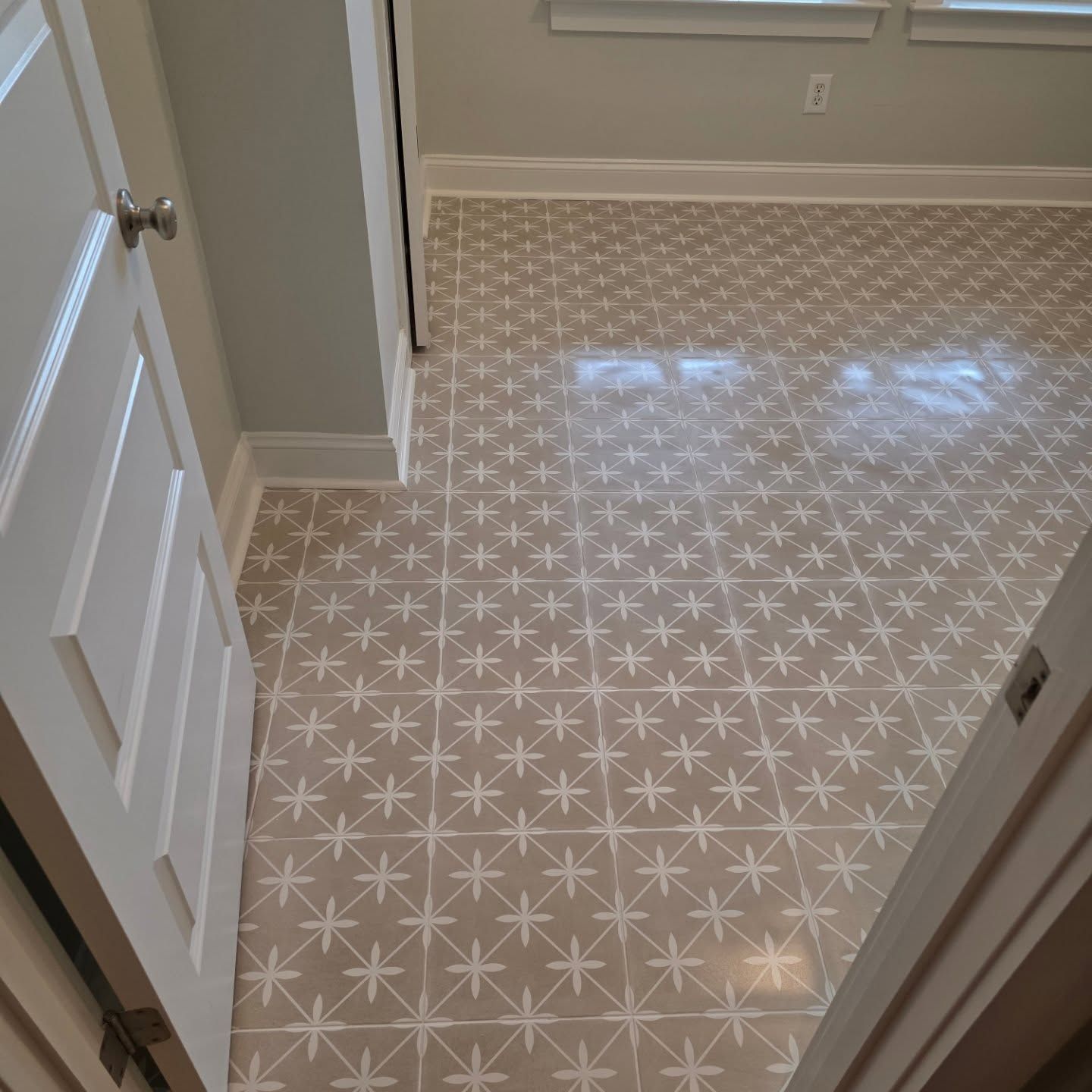 Small bathroom with light patterned tile floor and beige walls, viewed through an open door.