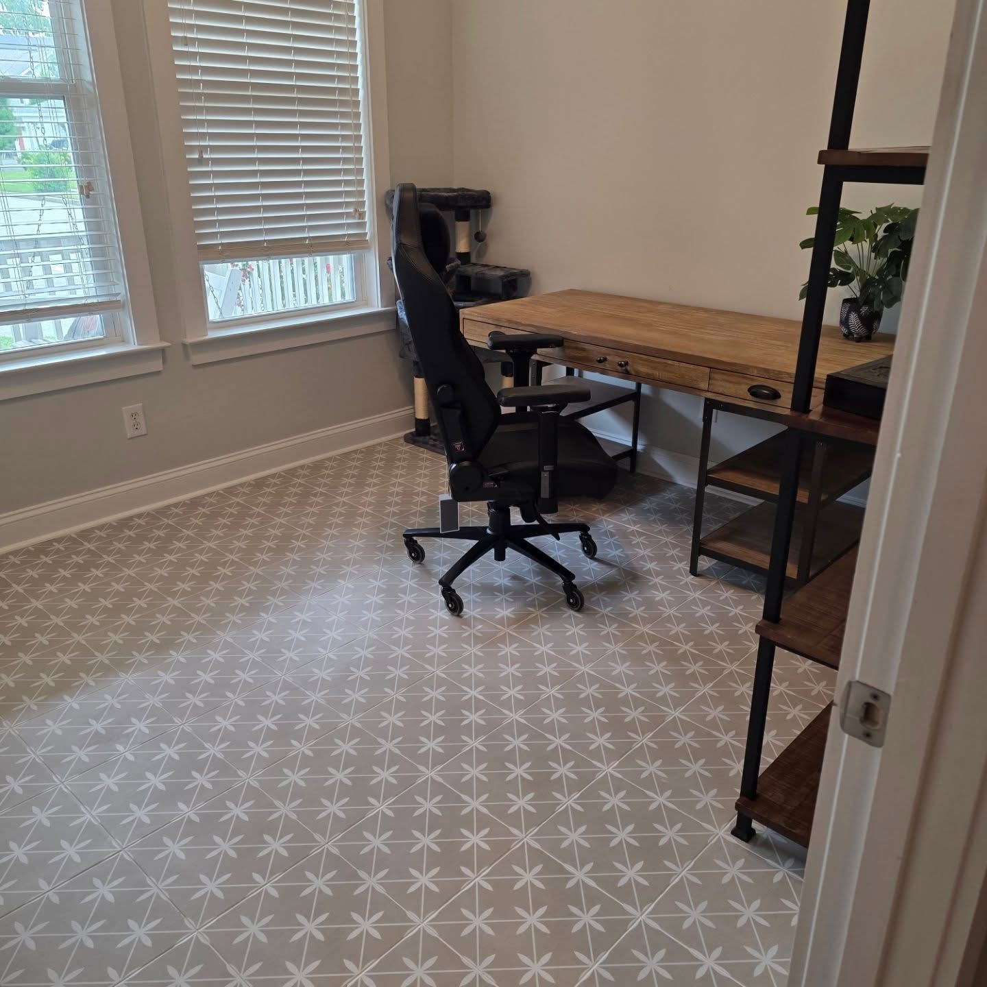 Small home office with desk, black chair, window blinds, and patterned carpet floor