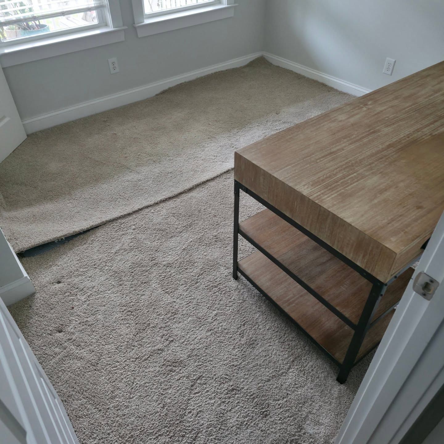 Empty carpeted room with windows and a wooden desk by the wall, viewed from the doorway