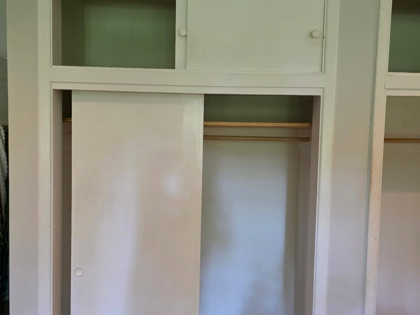 White sliding closet doors in a built-in wardrobe niche with hanging rod above.