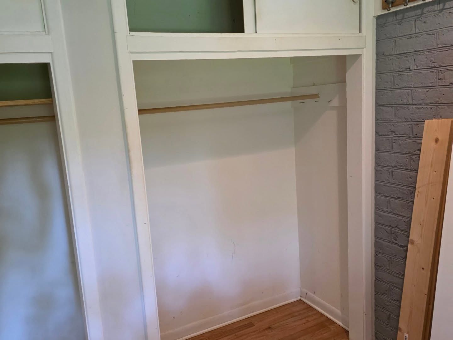 Empty white closet with built-in shelves, hanging rod, and wood floor in a room under construction