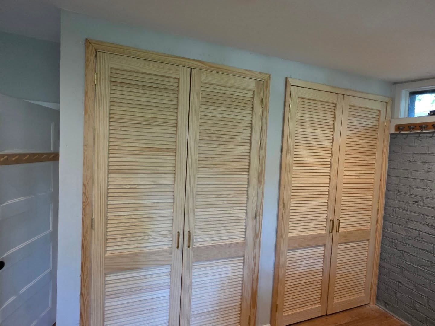 White louvered closet doors in a small room with tiled wall and brick accent wall.