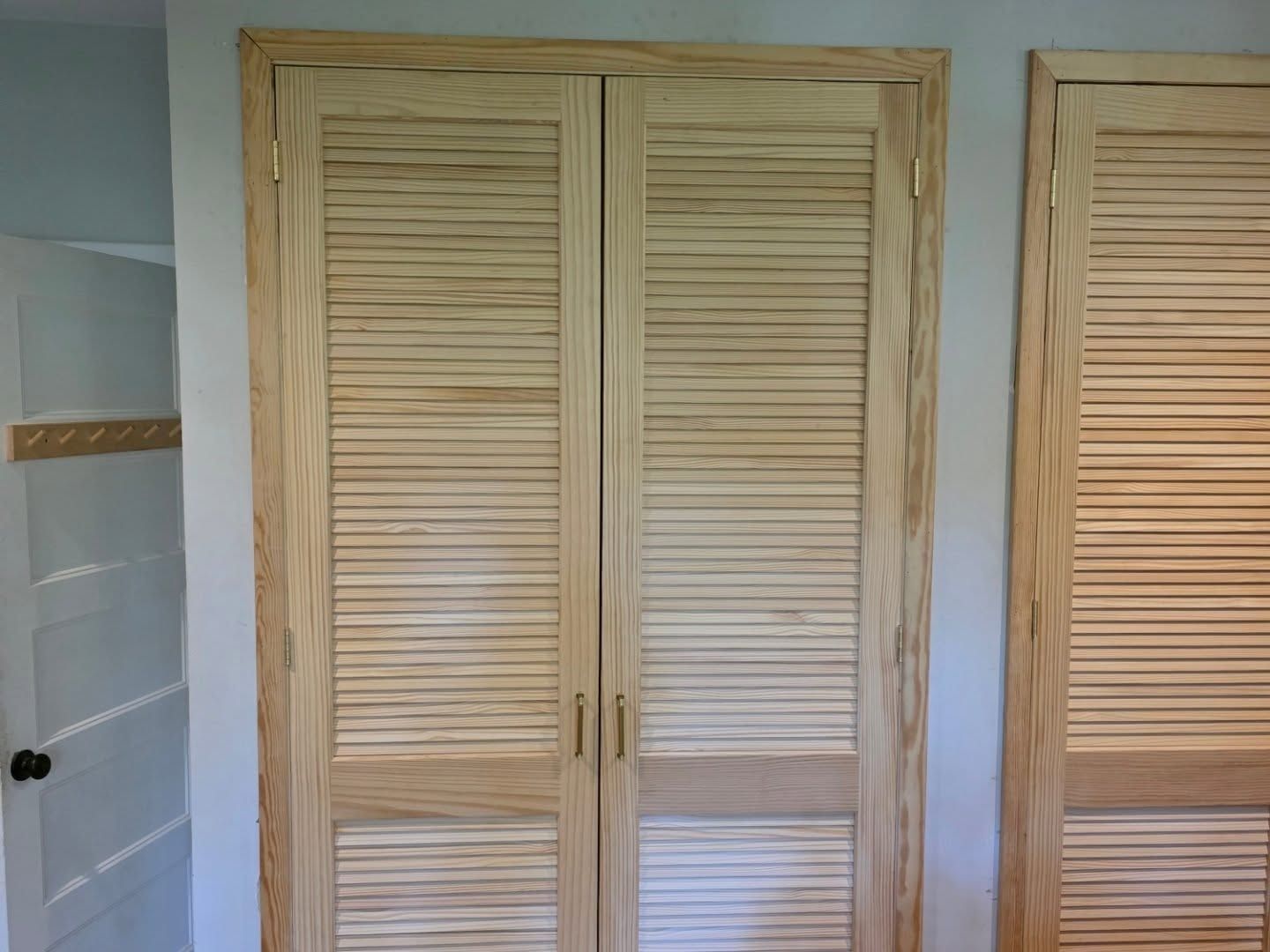 Wooden louvered closet doors in a tiled room, with part of a second door visible on the right