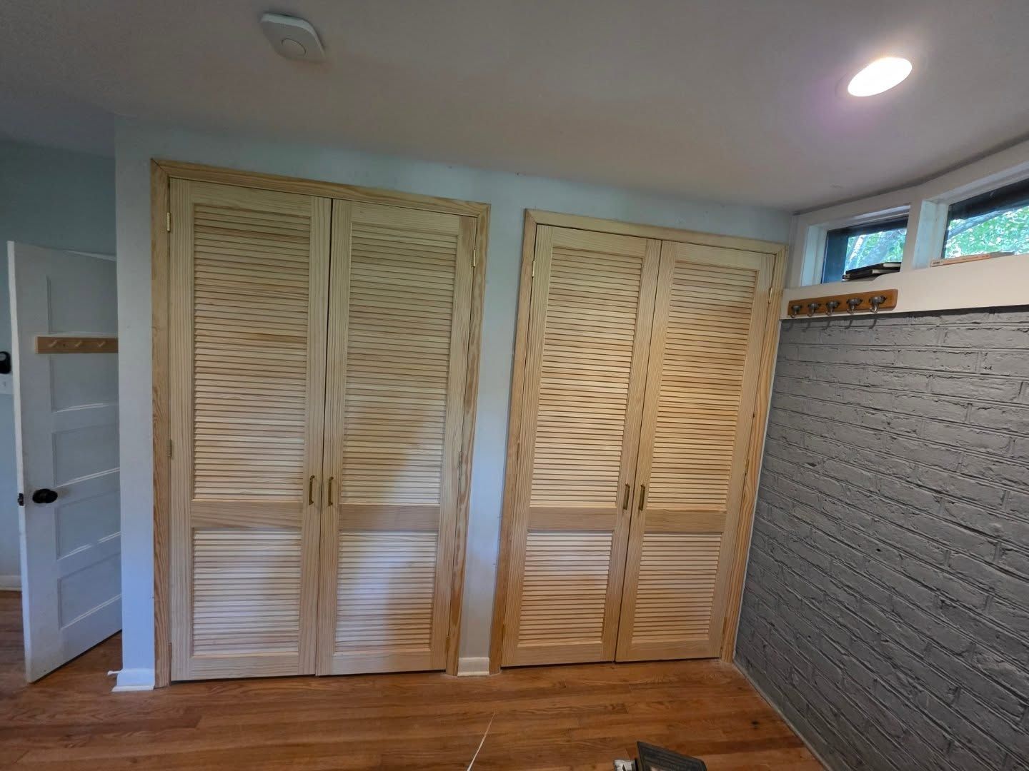 Small room with louvered wooden closet doors, hardwood floor, and a white brick accent wall.