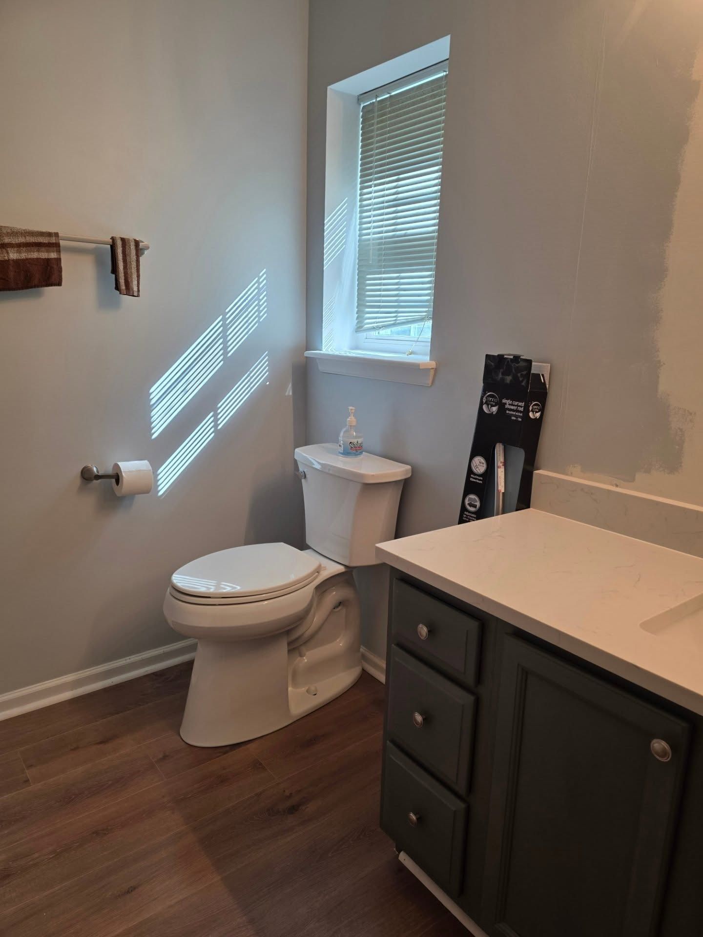 Small bathroom with toilet, window, dark vanity, and wood-look floor.