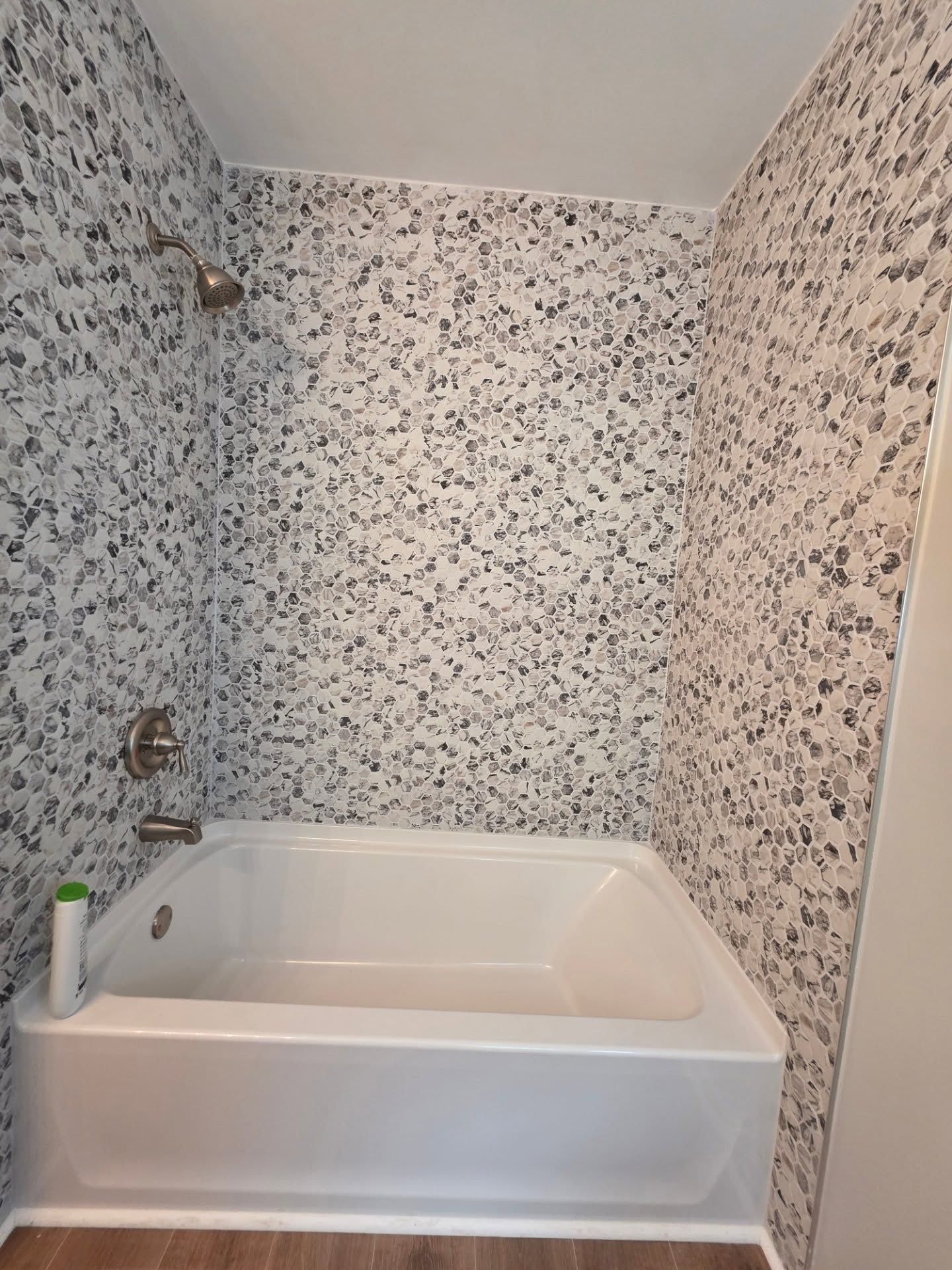 Small bathroom with a white bathtub, floral wallpaper, and a showerhead on the left wall.