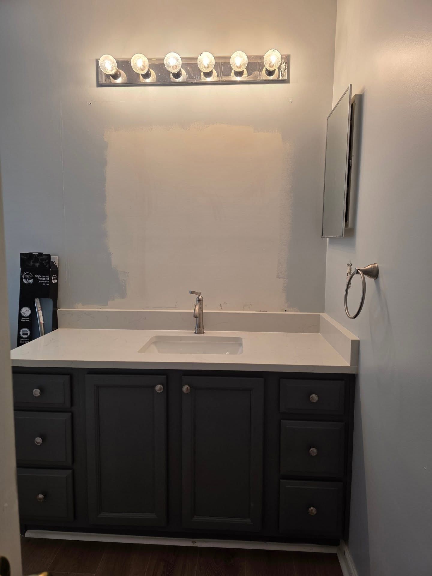 Small bathroom vanity with white countertop, black cabinet, and lit mirror lights above a sink.