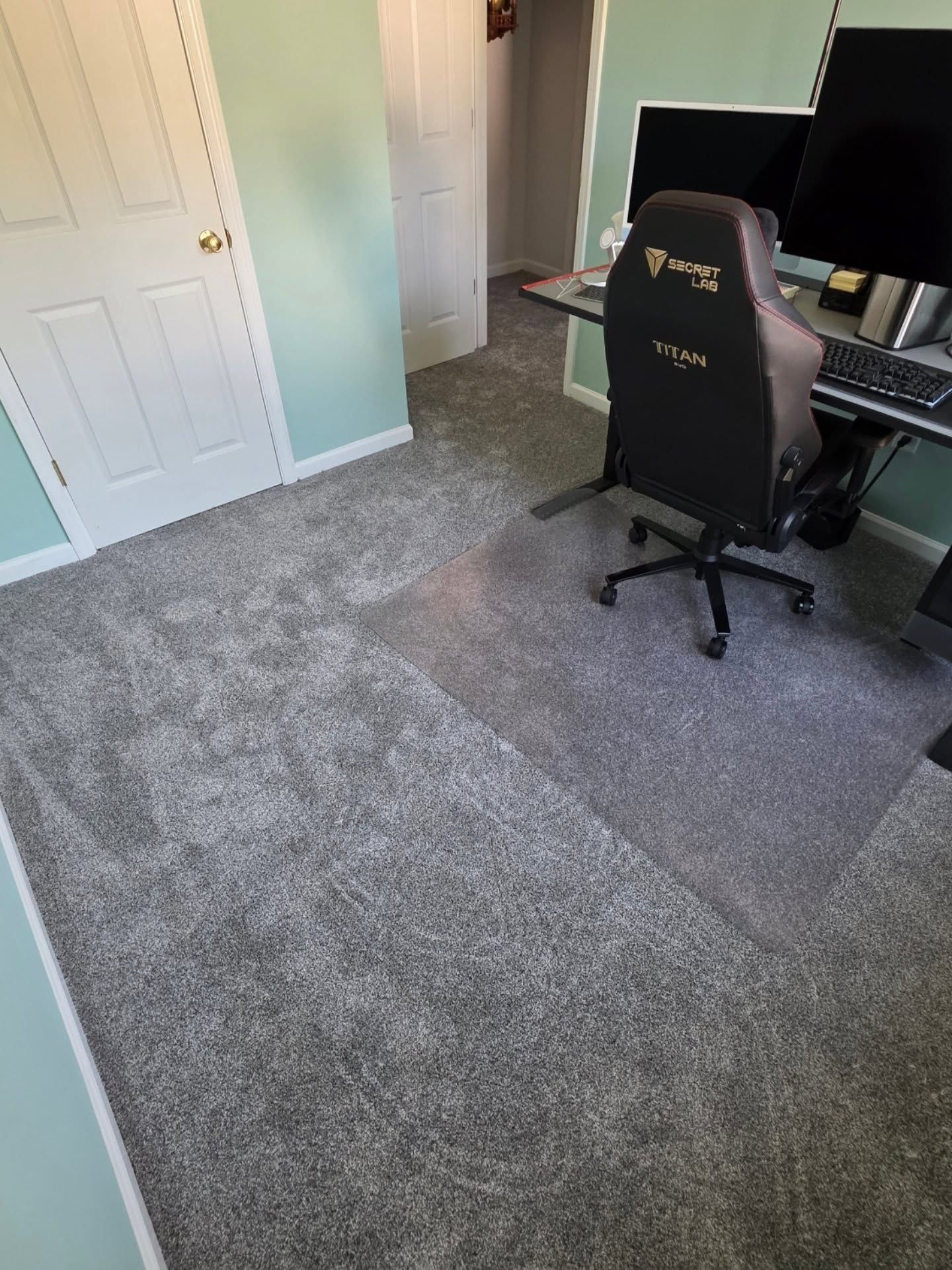 Carpeted home office with a black gaming chair, desk, computer monitors, and white doors.