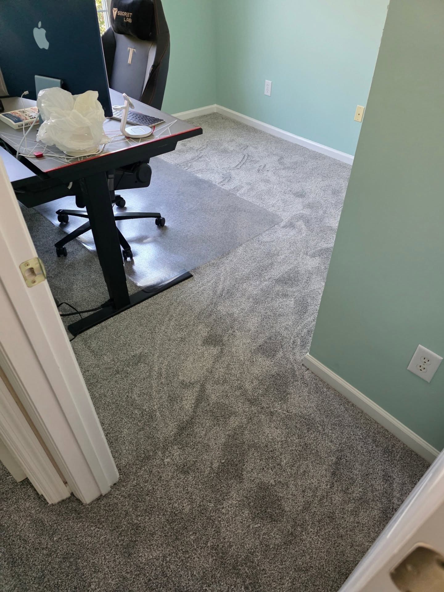 Empty office room with gray carpet, light blue walls, and a desk with papers near the doorway