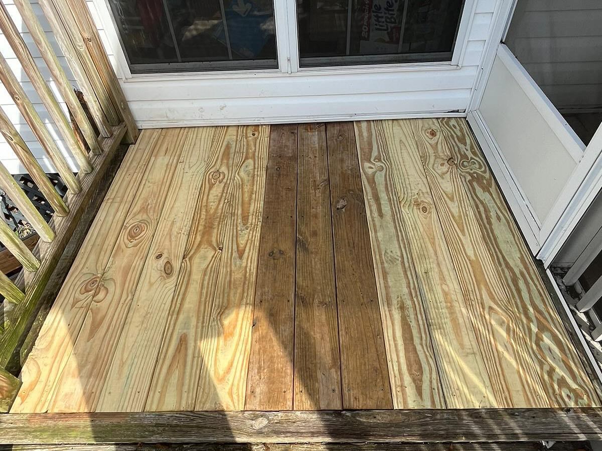 Wooden porch floor beside white railings and a screened door, lit by sunlight and shadow.