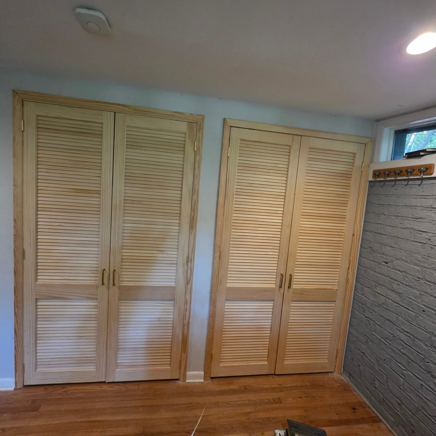 Two beige louvered closet doors in a room with wood floors and a ceiling light