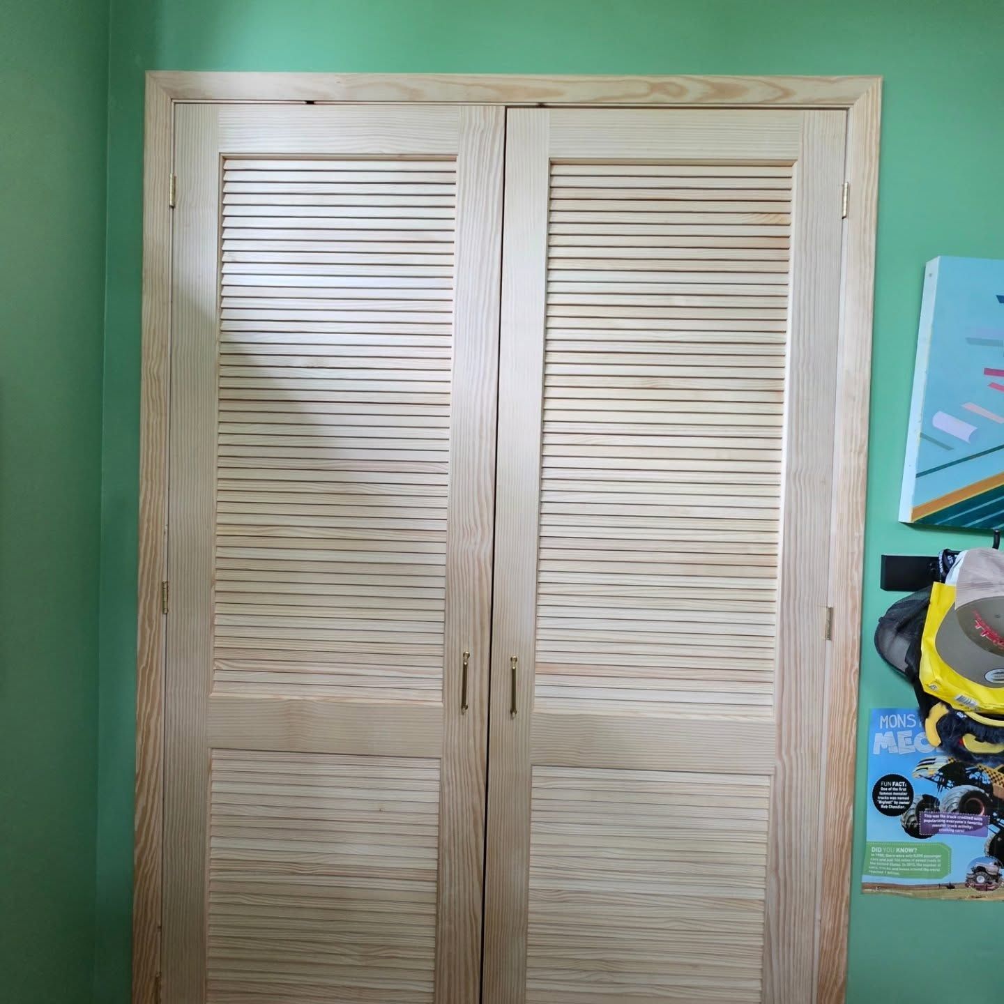 White louvered double closet doors against a green wall, with a colorful poster on the right.