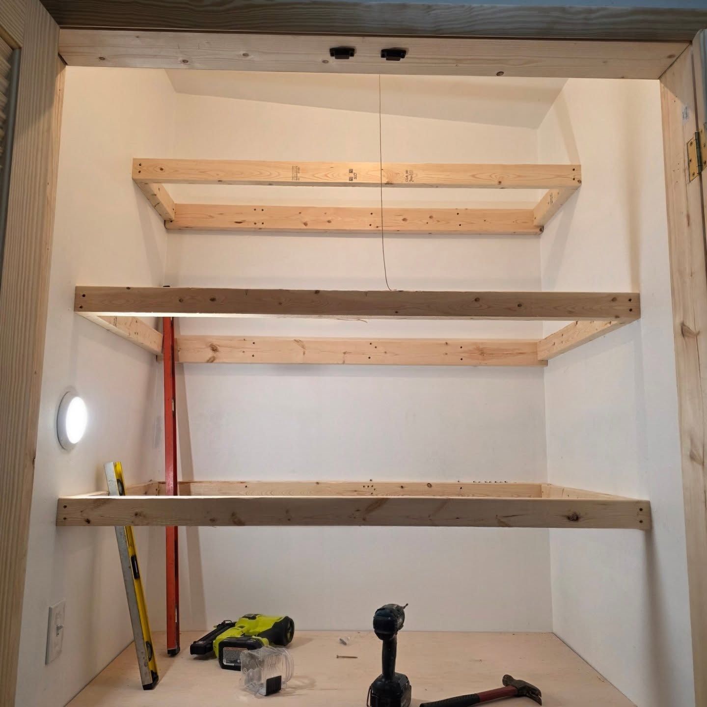 Partially built wooden shelves mounted in a small white closet under construction.