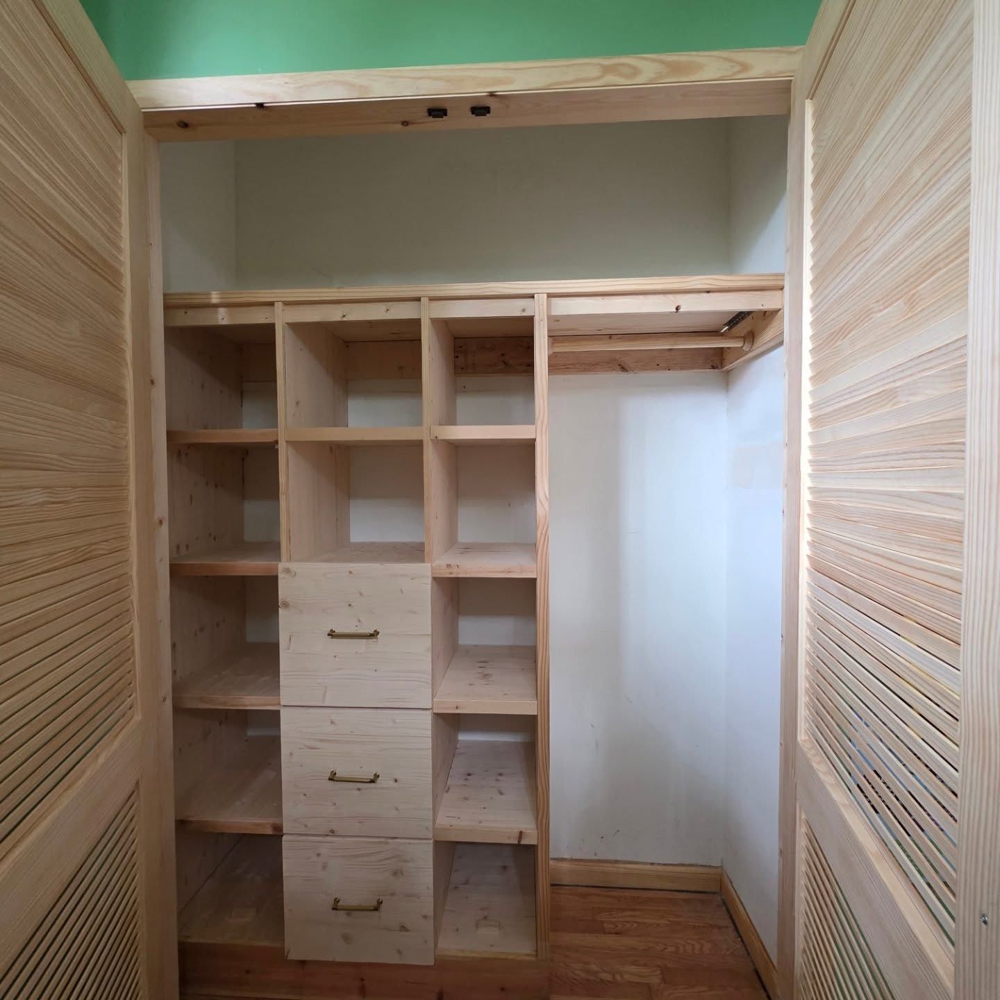 Empty closet with built-in cubbies, hanging rod, and louvered doors in a light wood finish