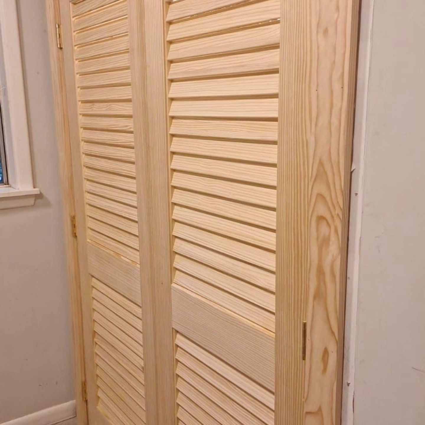 Wooden louvered closet doors with a light natural finish in a hallway.