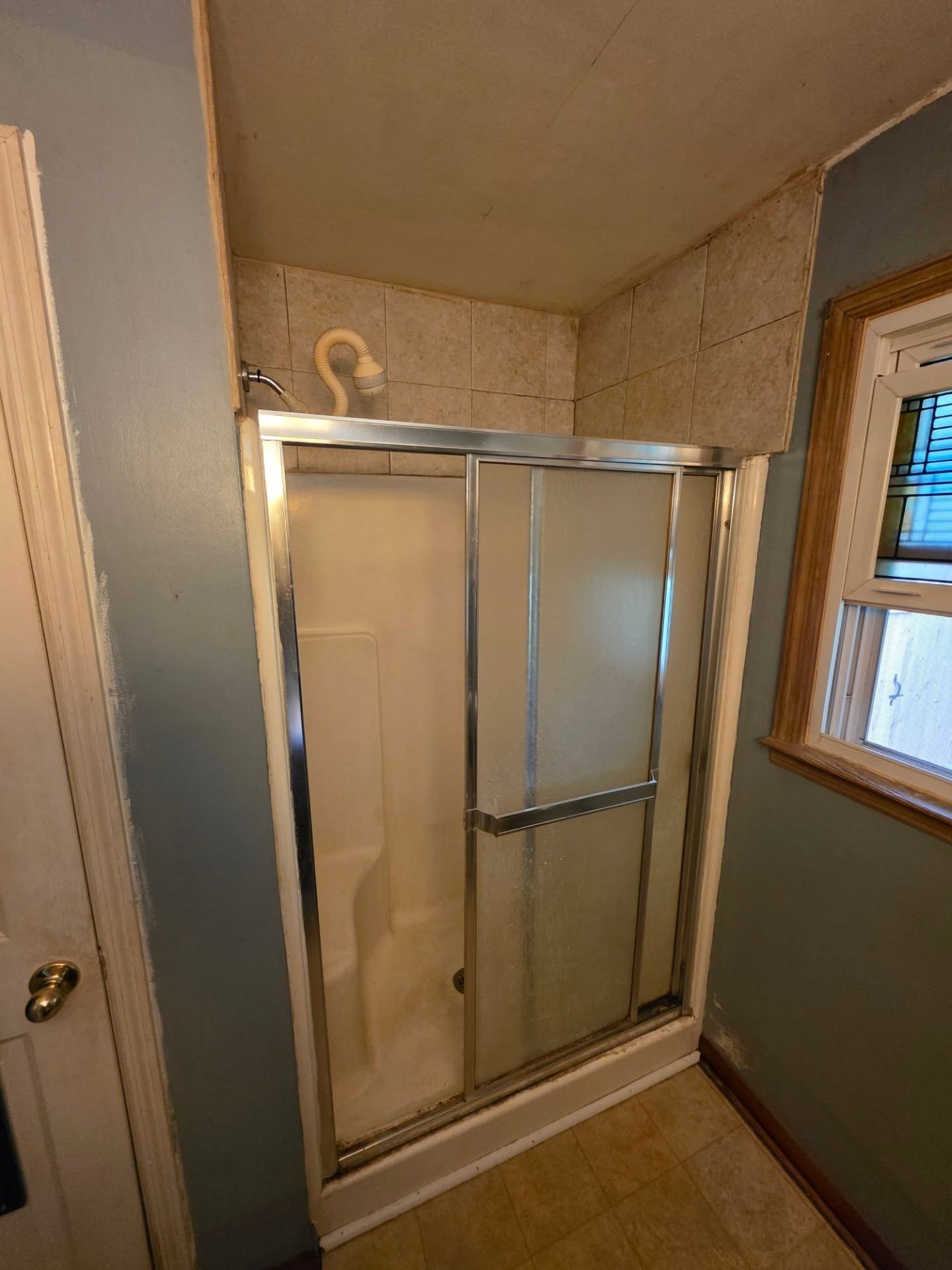 Bathroom shower with sliding glass doors and white tile walls in a small corner alcove