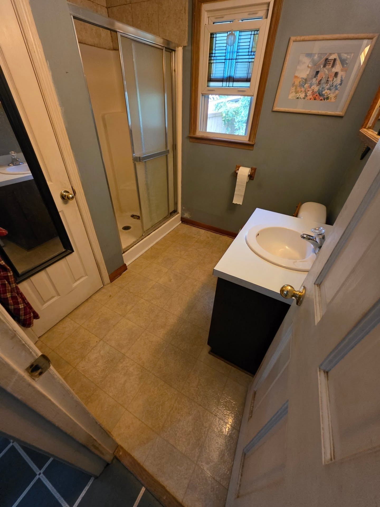 Small bathroom with shower, sink vanity, window, and beige tile floor.