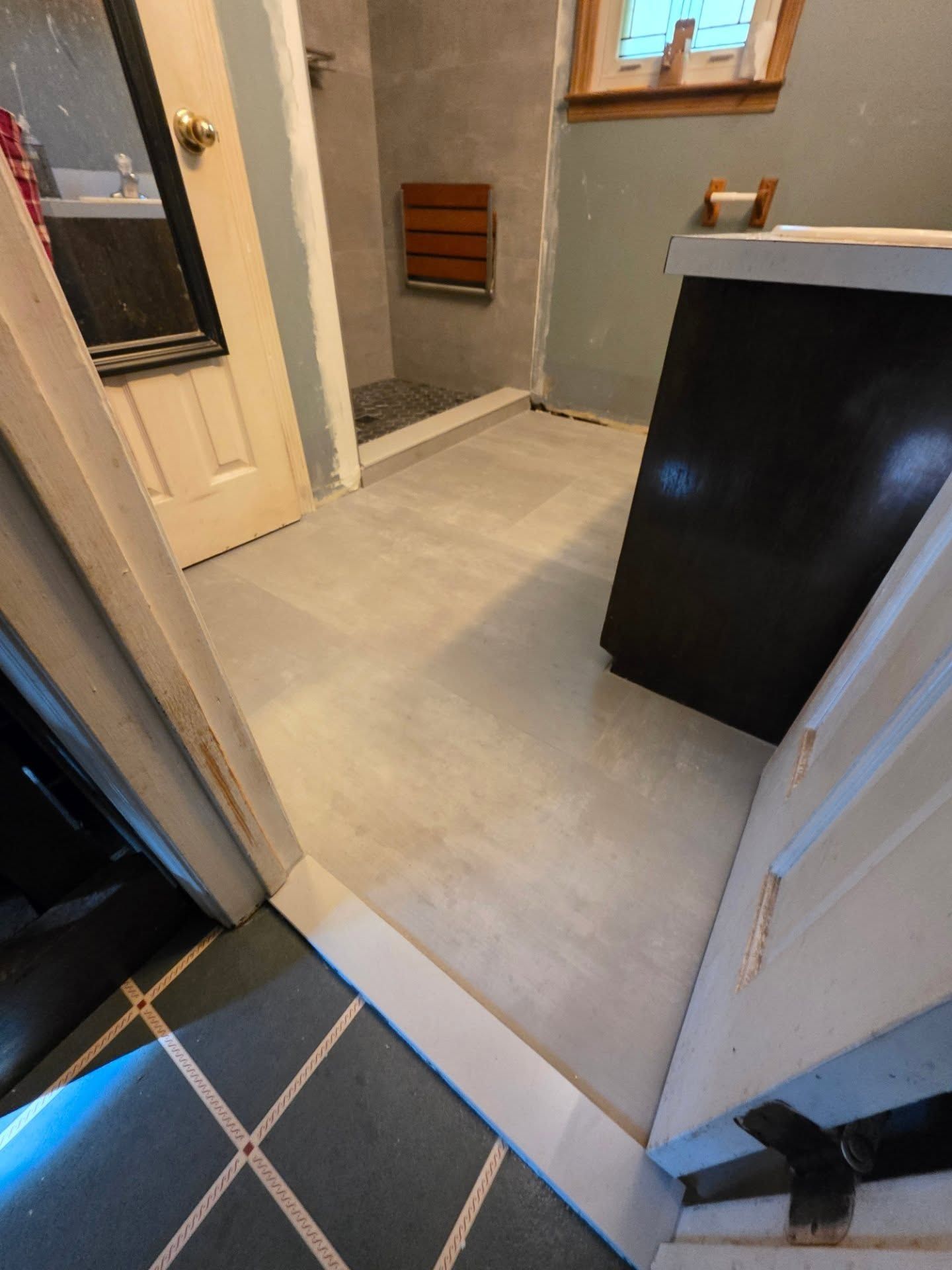 Small bathroom with tiled floor, sink cabinet, toilet, window, and shower area.