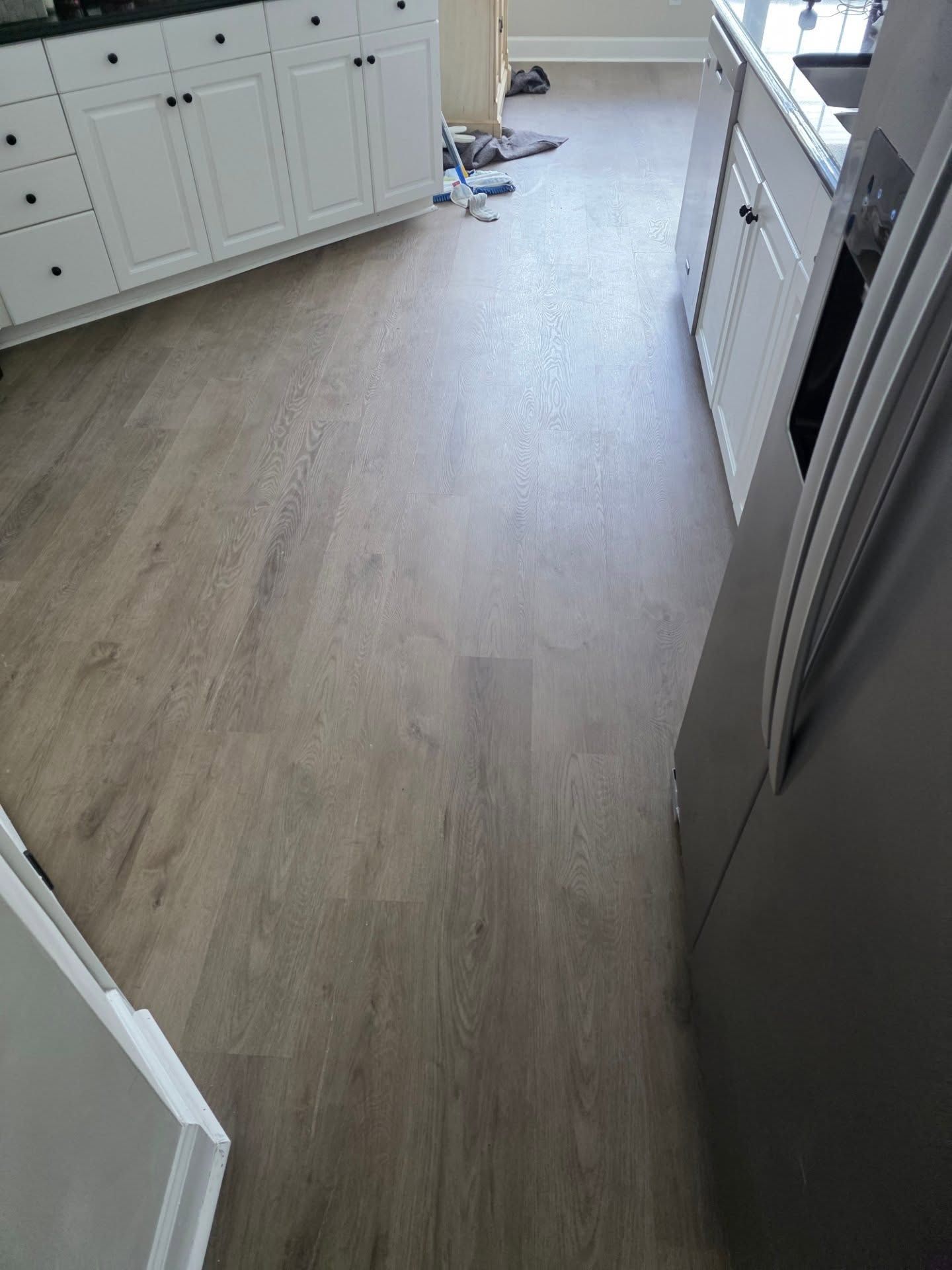 Light wood kitchen floor with white cabinets and a refrigerator on the right