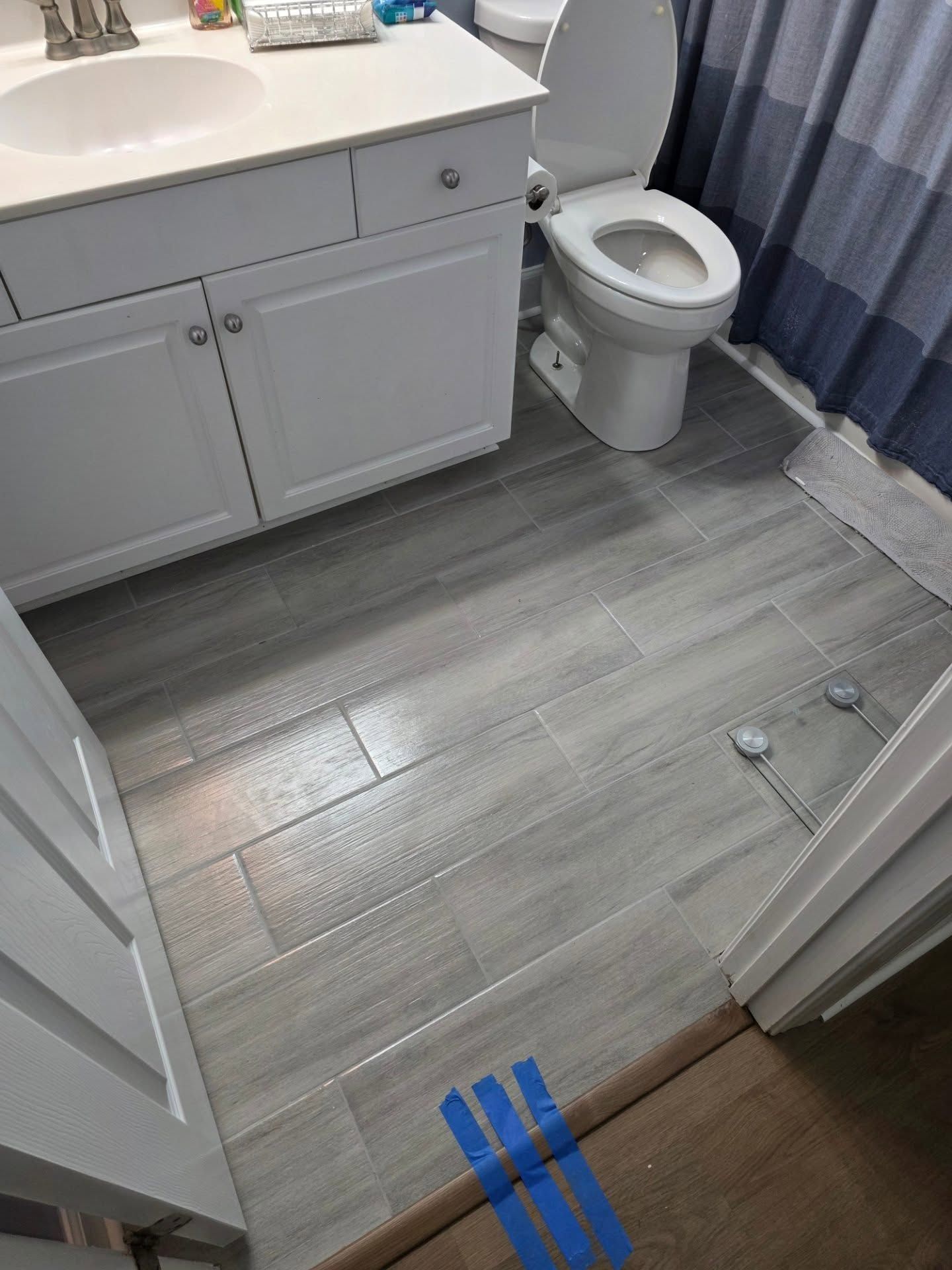 Accessible bathroom with sink, toilet, gray tile floor, and blue-striped curtain