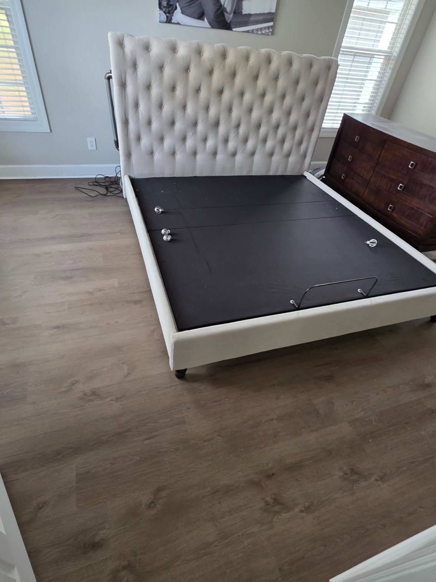 Bedroom with a tufted beige headboard and bed frame, dark mattress, wood floor, and dresser nearby