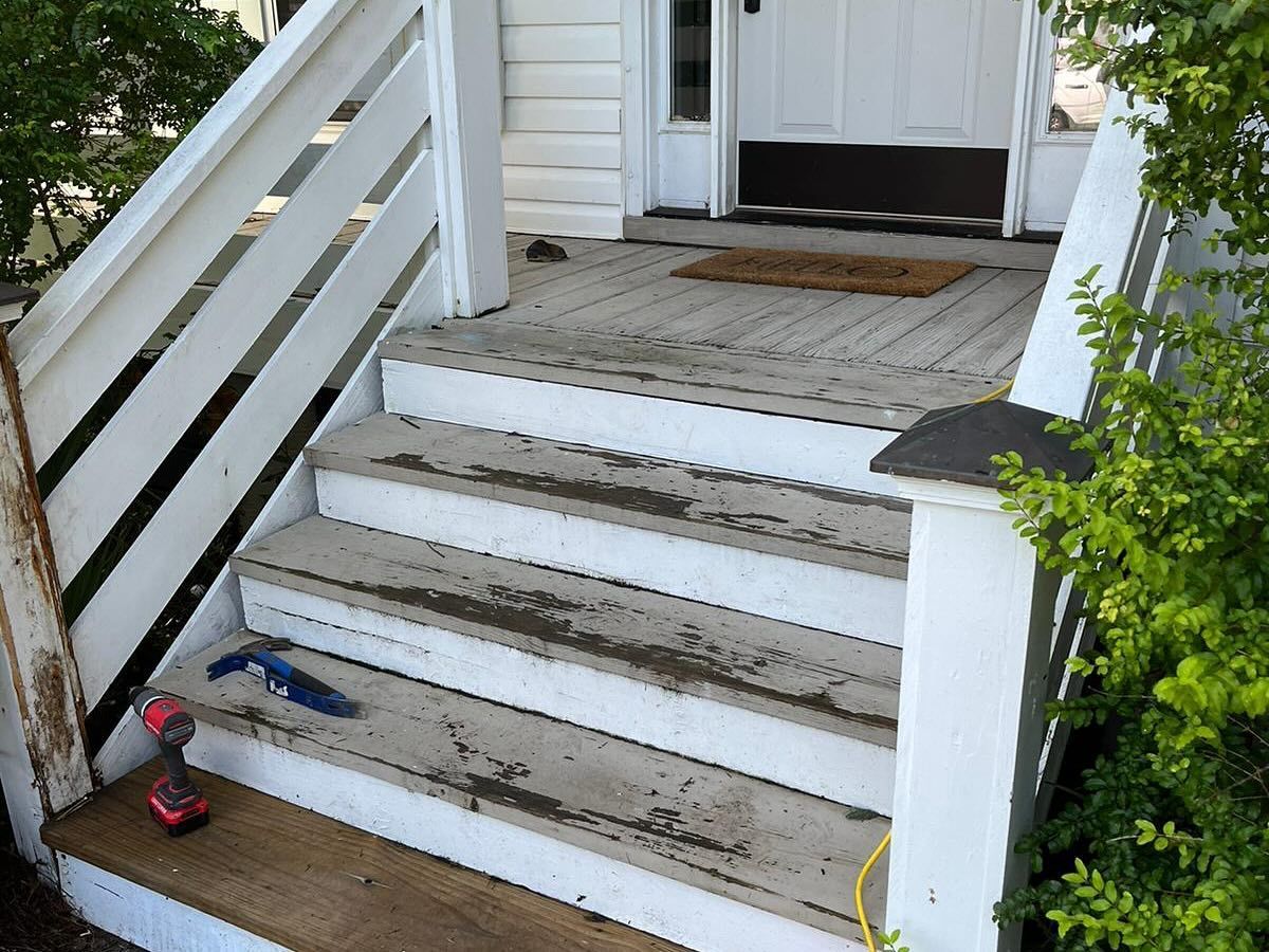 Front steps with a white railing, worn white stairs, and tools resting on the porch near a white door