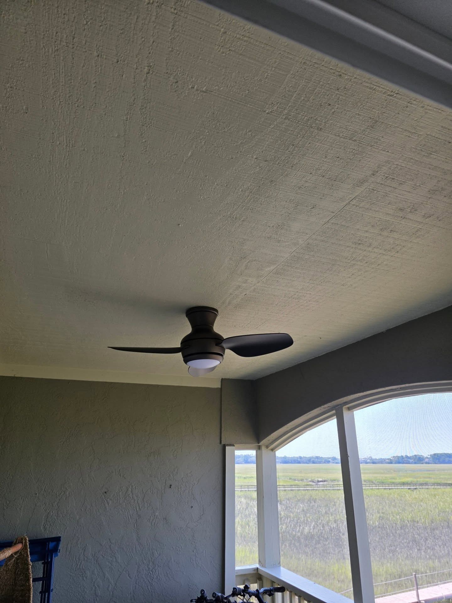 Covered patio ceiling with a black ceiling fan and large screened windows overlooking a grassy yard