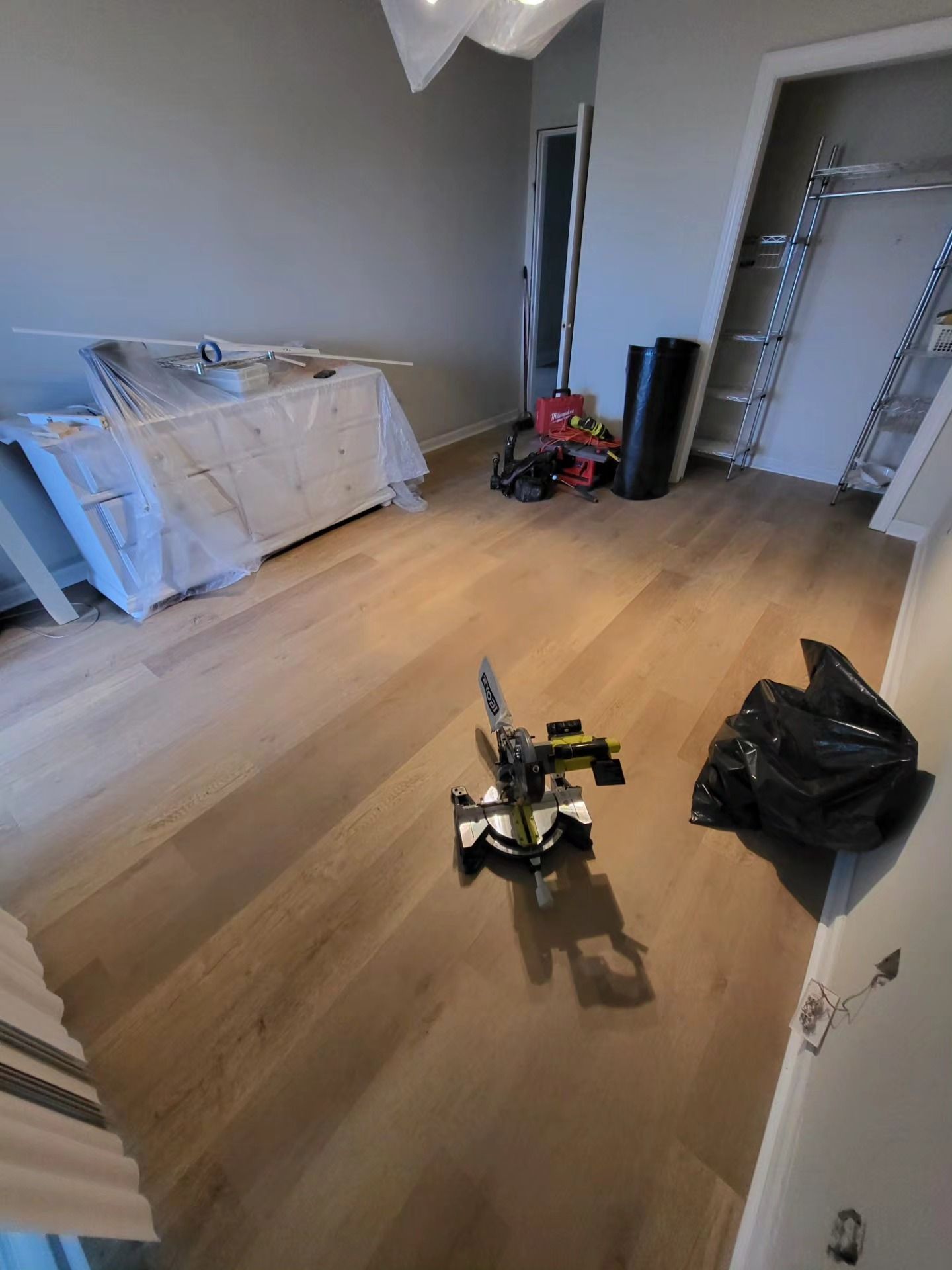 Empty room with hardwood floor, boxed furniture, and a small robot toy in the center.