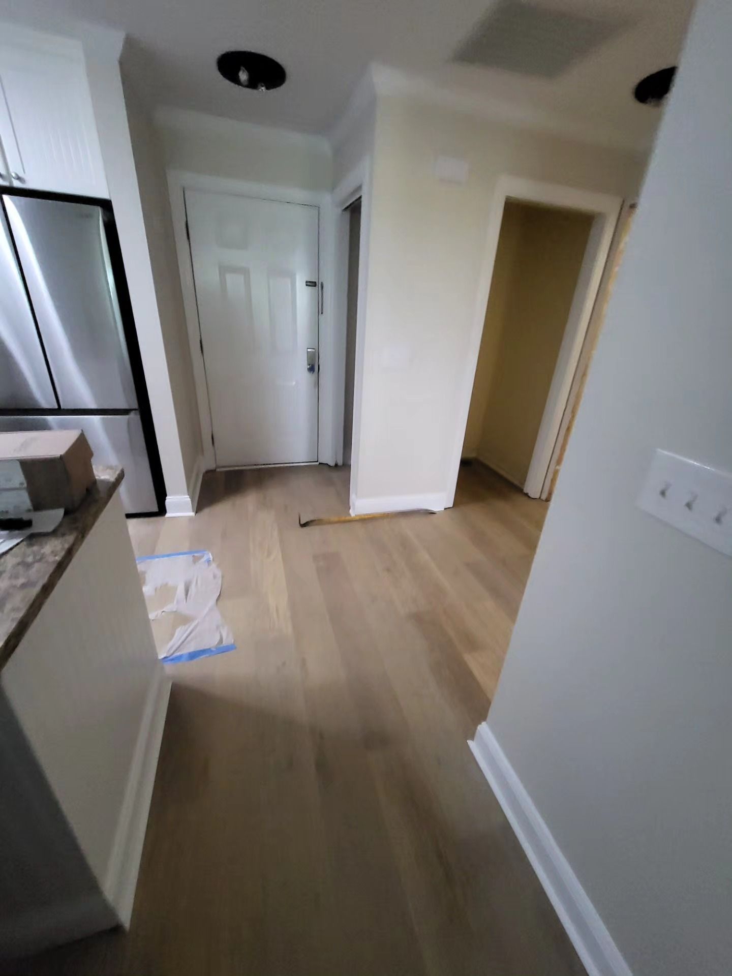 Empty hallway with light wood floors, white doors, and a kitchen edge on the left.